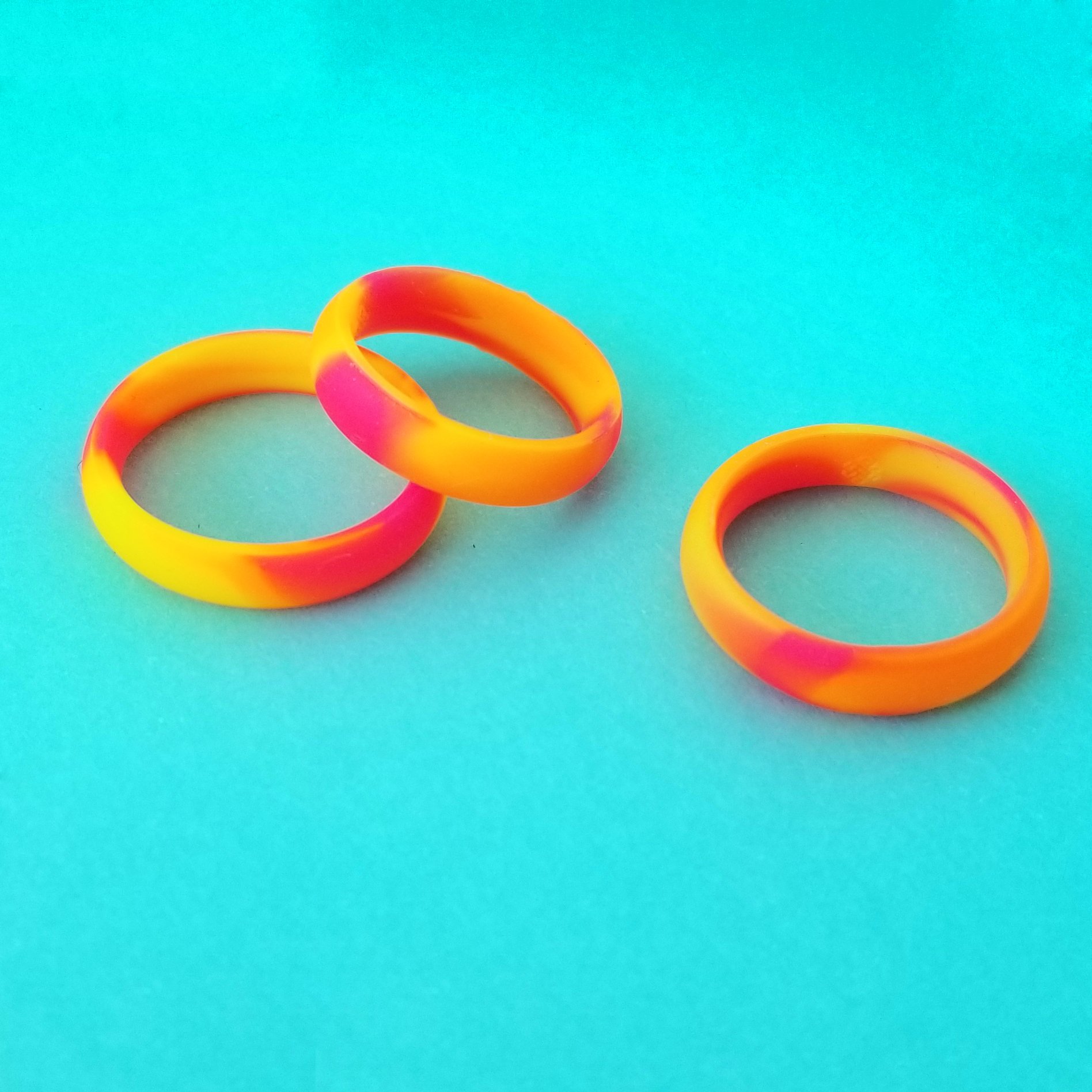 Vibrant neon orange, yellow, and pink swirl silicone ring with a sleek bevel design, showcasing its breathable and comfortable fit.