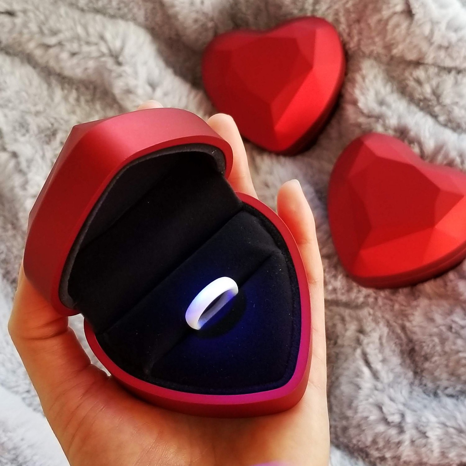 A luxurious red heart-shaped ring box with a satin finish and midnight blue velvet lining, designed to illuminate the ring inside when opened.