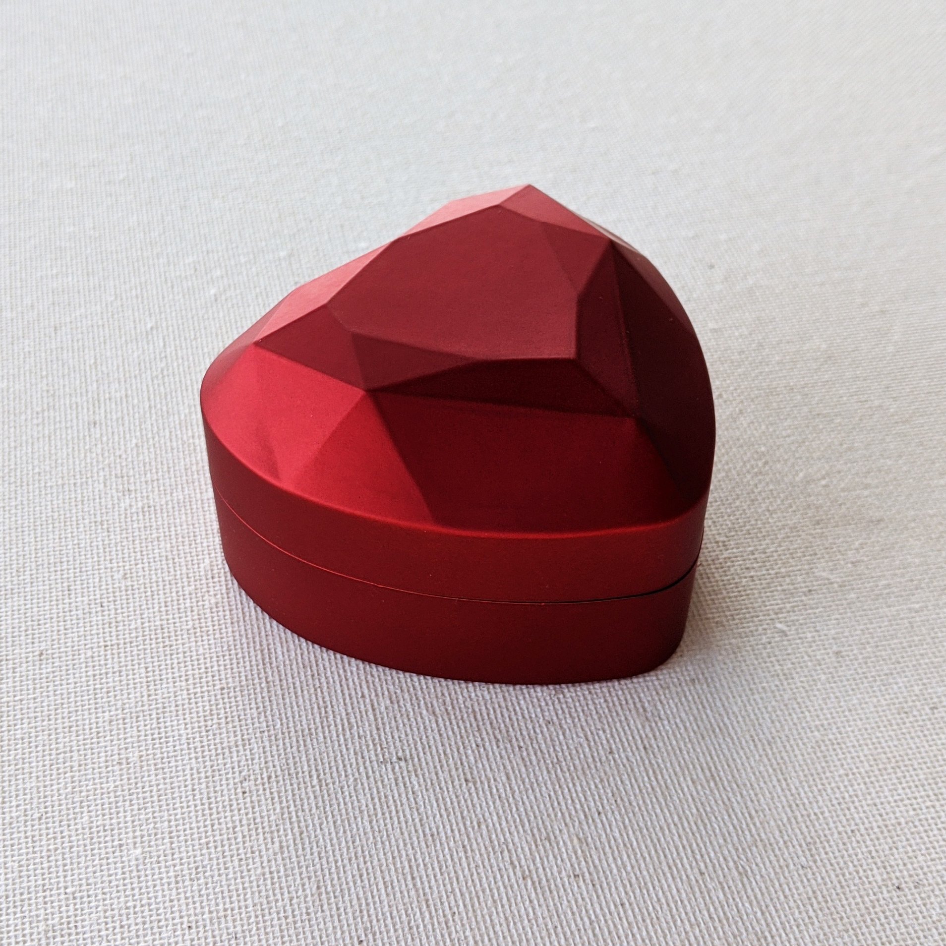 A luxurious red heart-shaped ring box with a satin finish and midnight blue velvet lining, designed to illuminate the ring inside when opened.