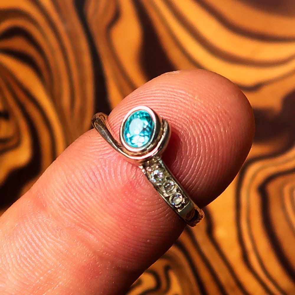 Sterling Silver Solitaire Band Ring featuring an oval cut blue Zircon and three cubic zirconia stones, polished to a mirror finish.