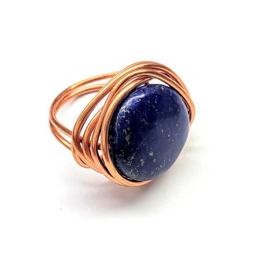 A handcrafted wire wrapped copper ring featuring a deep blue lapis lazuli coin bead, showcasing unique design and sparkling pyrite speckles.