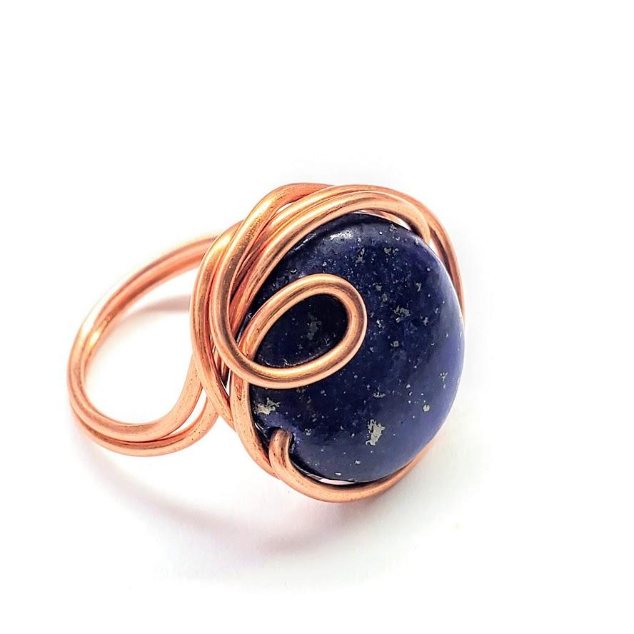 A handcrafted wire wrapped copper ring featuring a deep blue lapis lazuli coin bead, showcasing unique design and sparkling pyrite speckles.