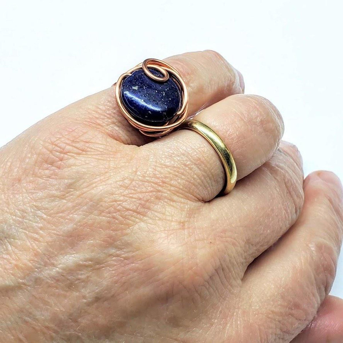 A handcrafted wire wrapped copper ring featuring a deep blue lapis lazuli coin bead, showcasing unique design and sparkling pyrite speckles.