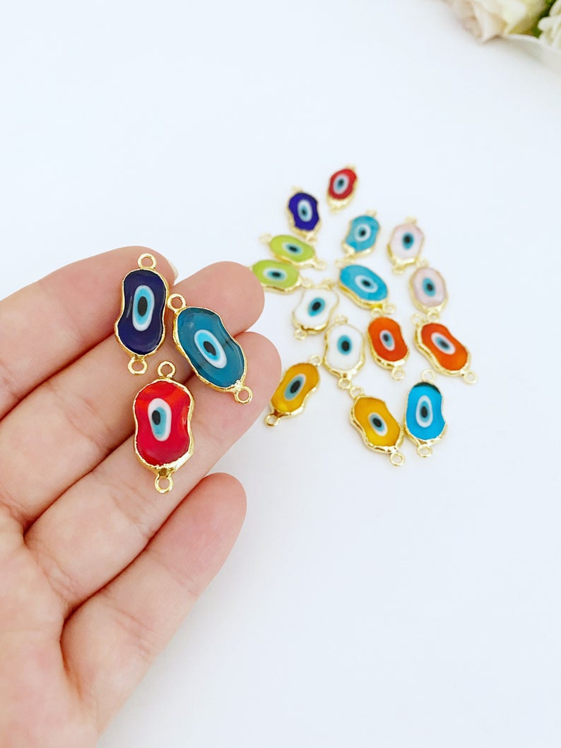 A collection of handmade Evil Eye Murano beads in various colors, showcasing their unique designs and 22K gold plated finish.