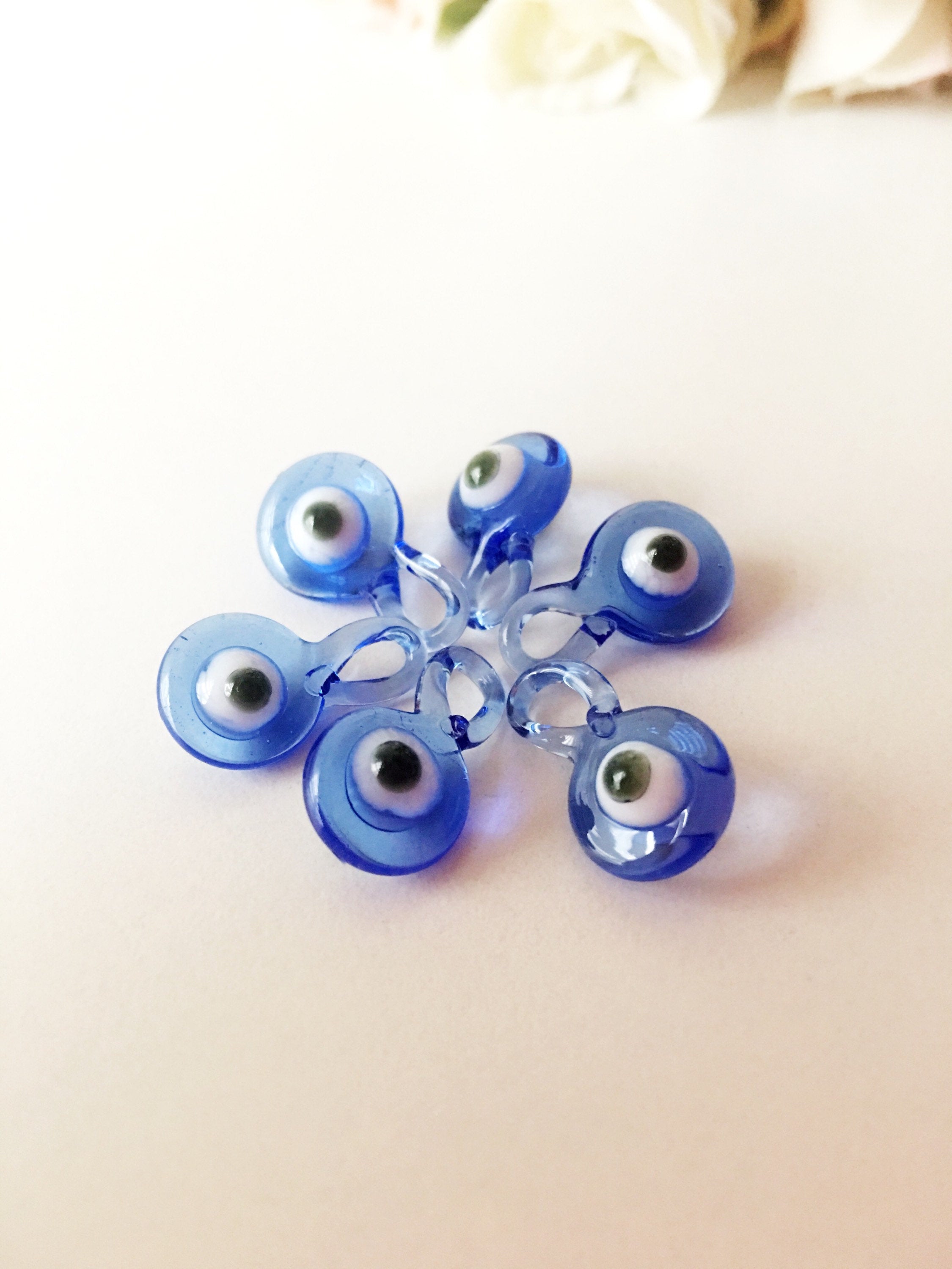 A collection of 10 blue glass evil eye charms, featuring intricate designs and metal hooks, perfect for baby shower favors.