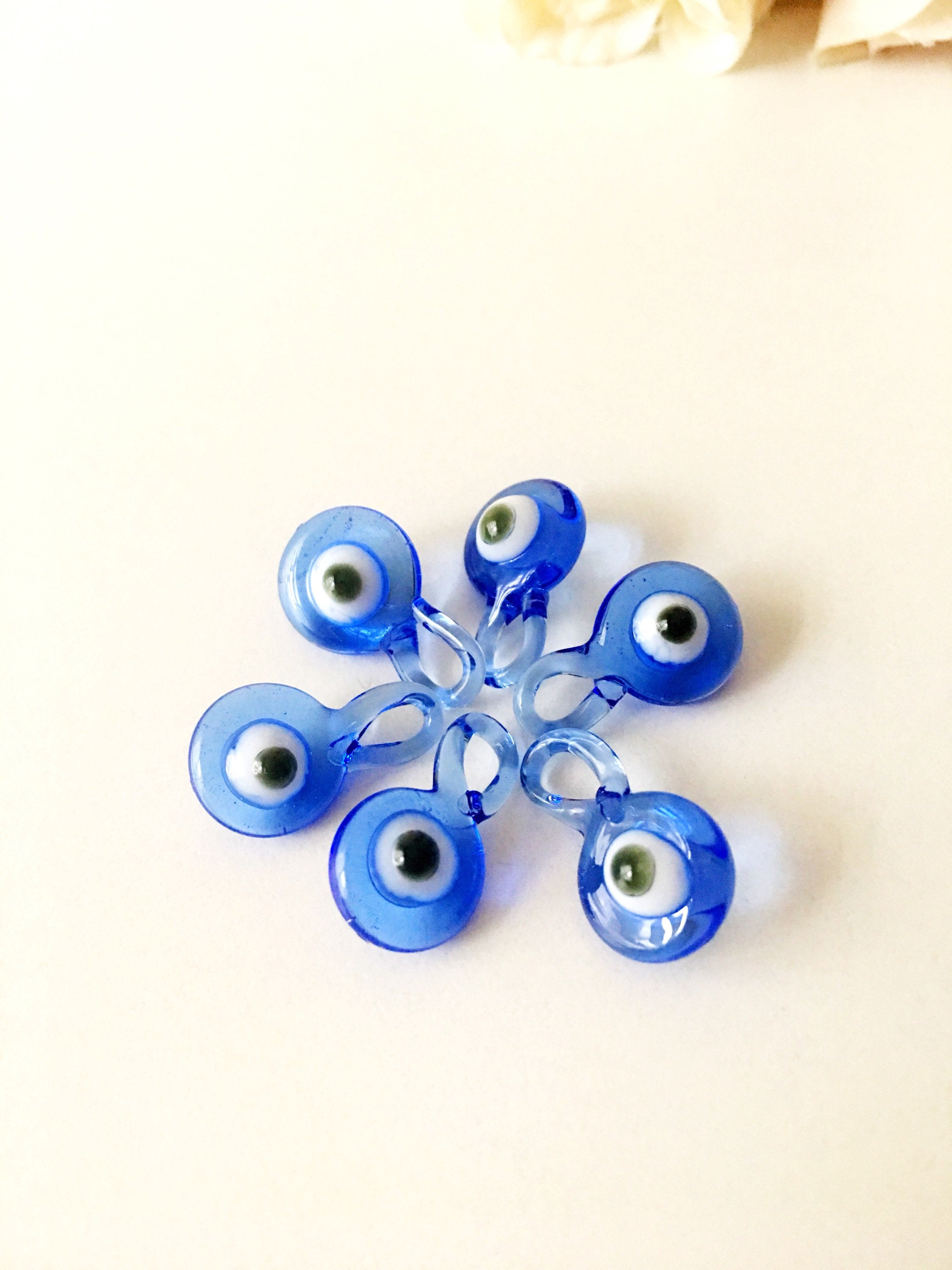 A collection of 10 blue glass evil eye charms, featuring intricate designs and metal hooks, perfect for baby shower favors.