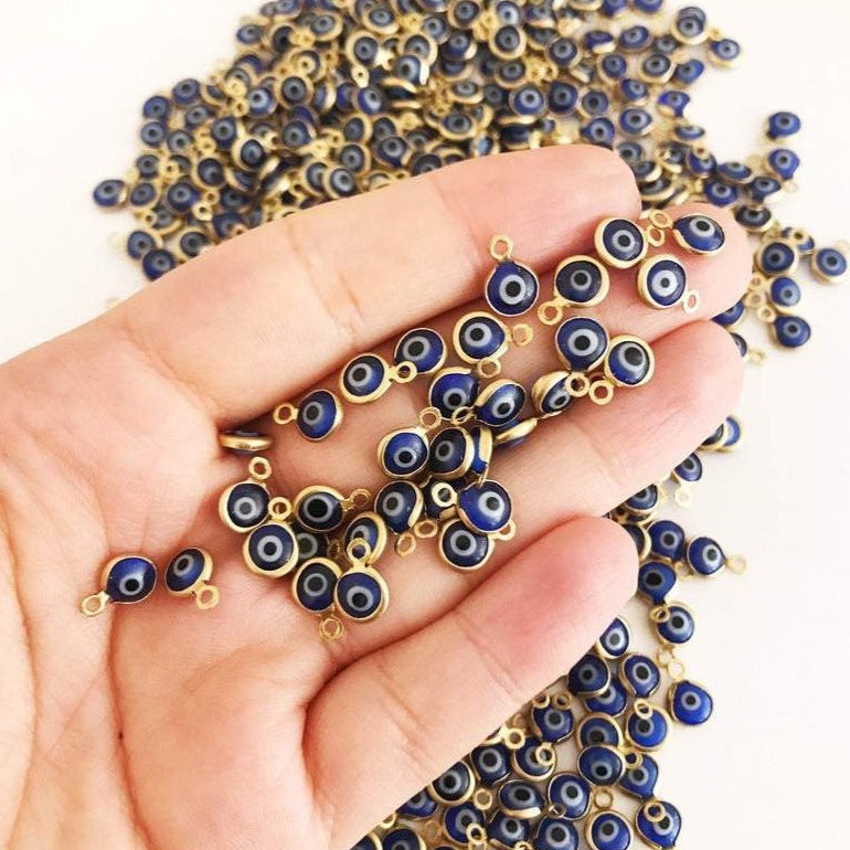 A bulk set of 100 blue evil eye beads, each 6mm in diameter, made from glass with stainless steel gold accents, showcasing both-sided charm design.