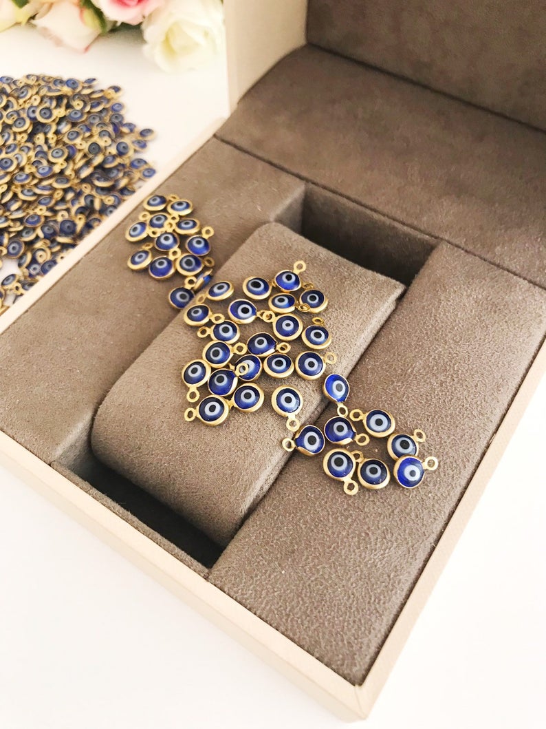 A bulk set of 100 blue evil eye beads, each 6mm in diameter, made from glass with stainless steel gold accents, showcasing both-sided charm design.