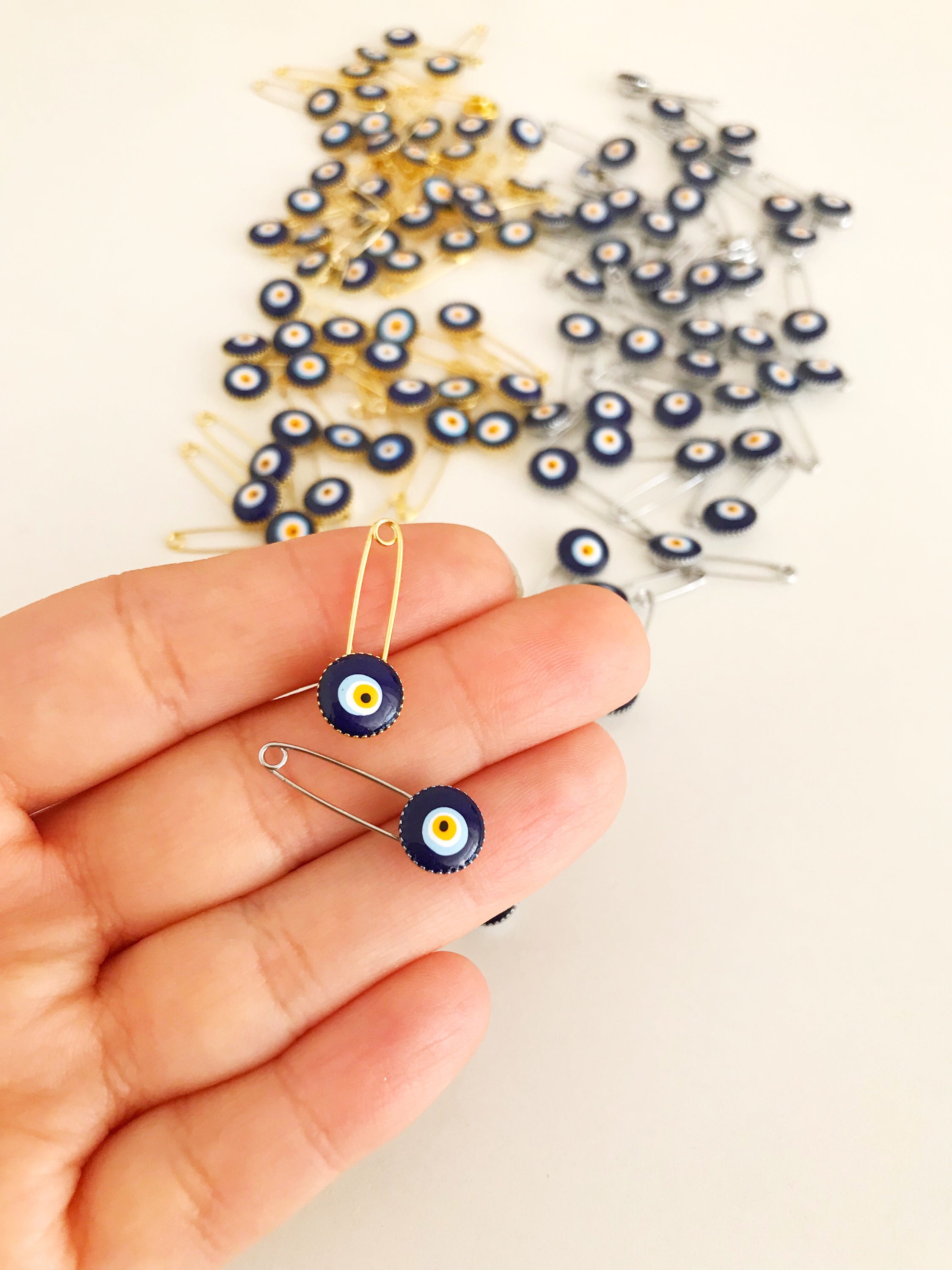 A collection of 100 blue evil eye safety pins, featuring brass construction and blue evil eye beads, ideal for weddings and baby showers.