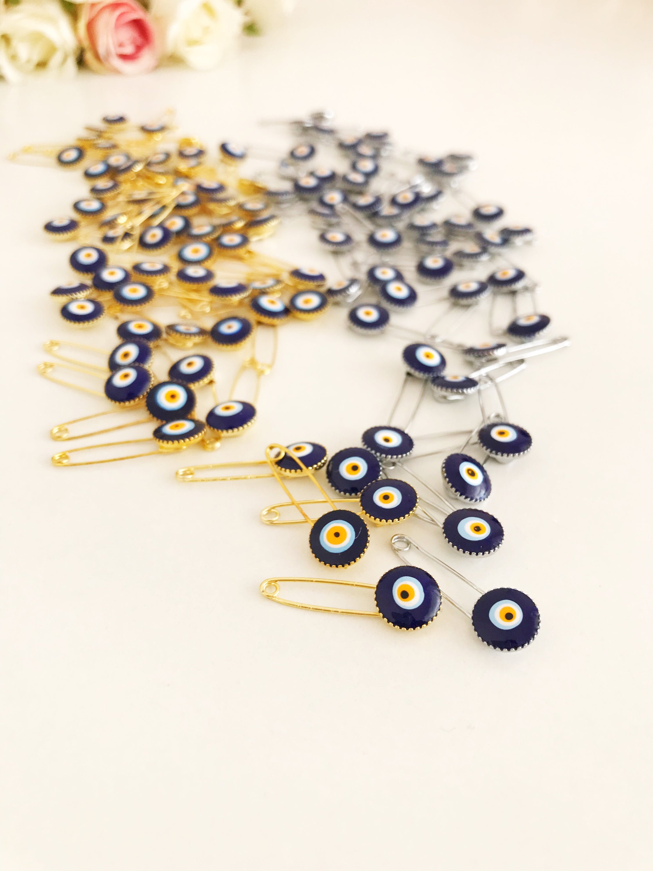 A collection of 100 blue evil eye safety pins, featuring brass construction and blue evil eye beads, ideal for weddings and baby showers.