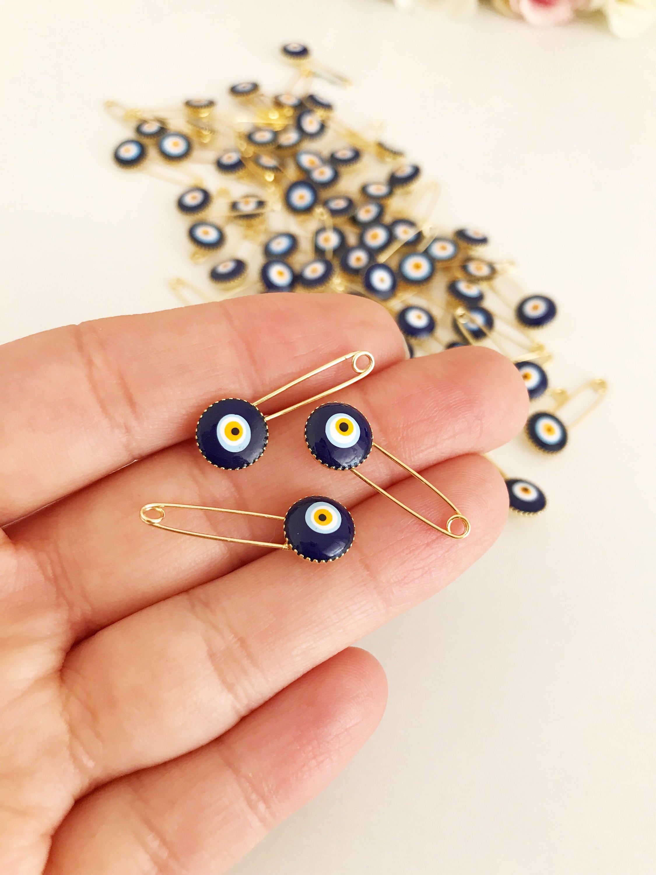 A collection of 100 blue evil eye safety pins, featuring brass construction and blue evil eye beads, ideal for weddings and baby showers.