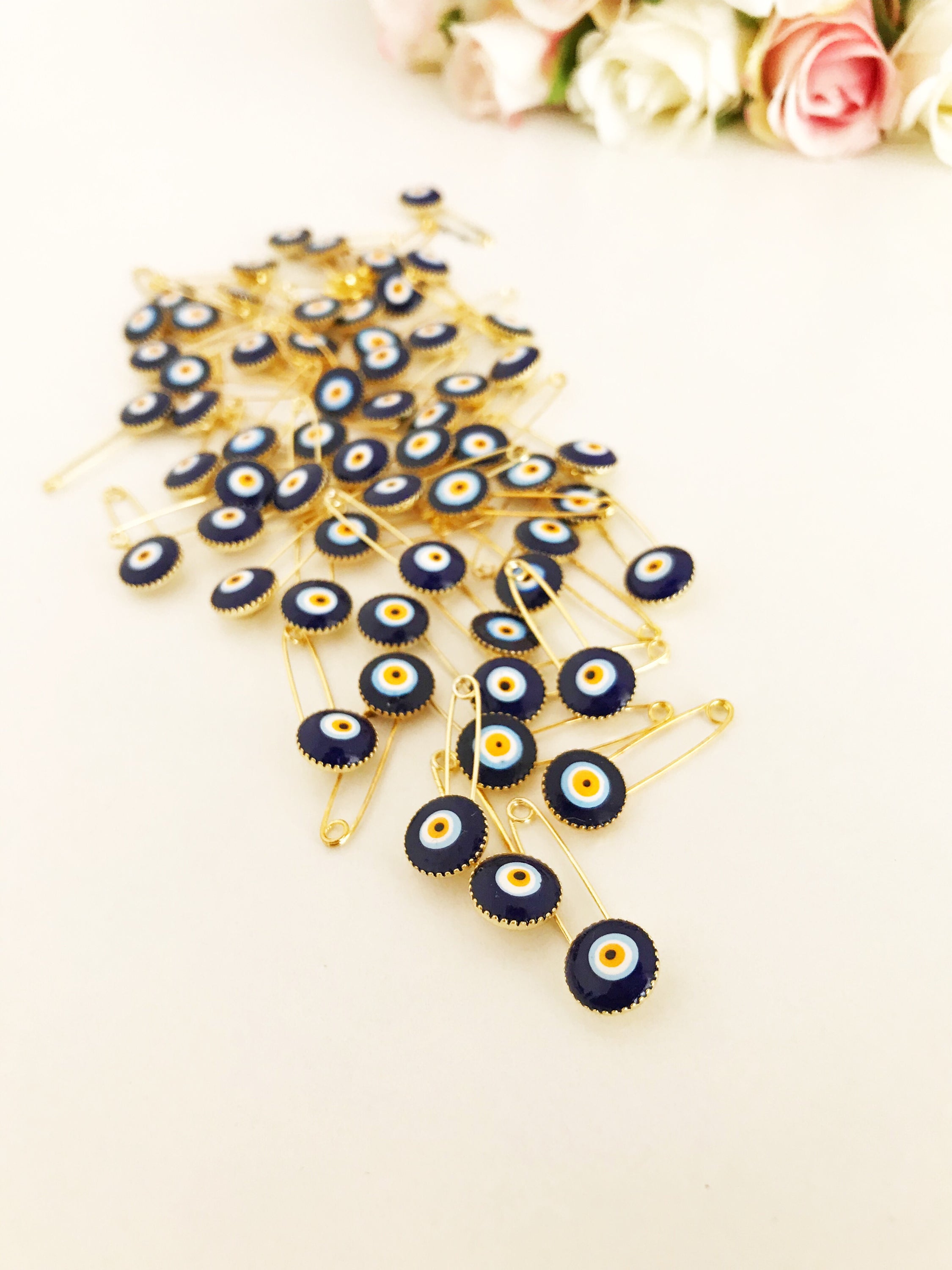 A collection of 100 blue evil eye safety pins, featuring brass construction and blue evil eye beads, ideal for weddings and baby showers.