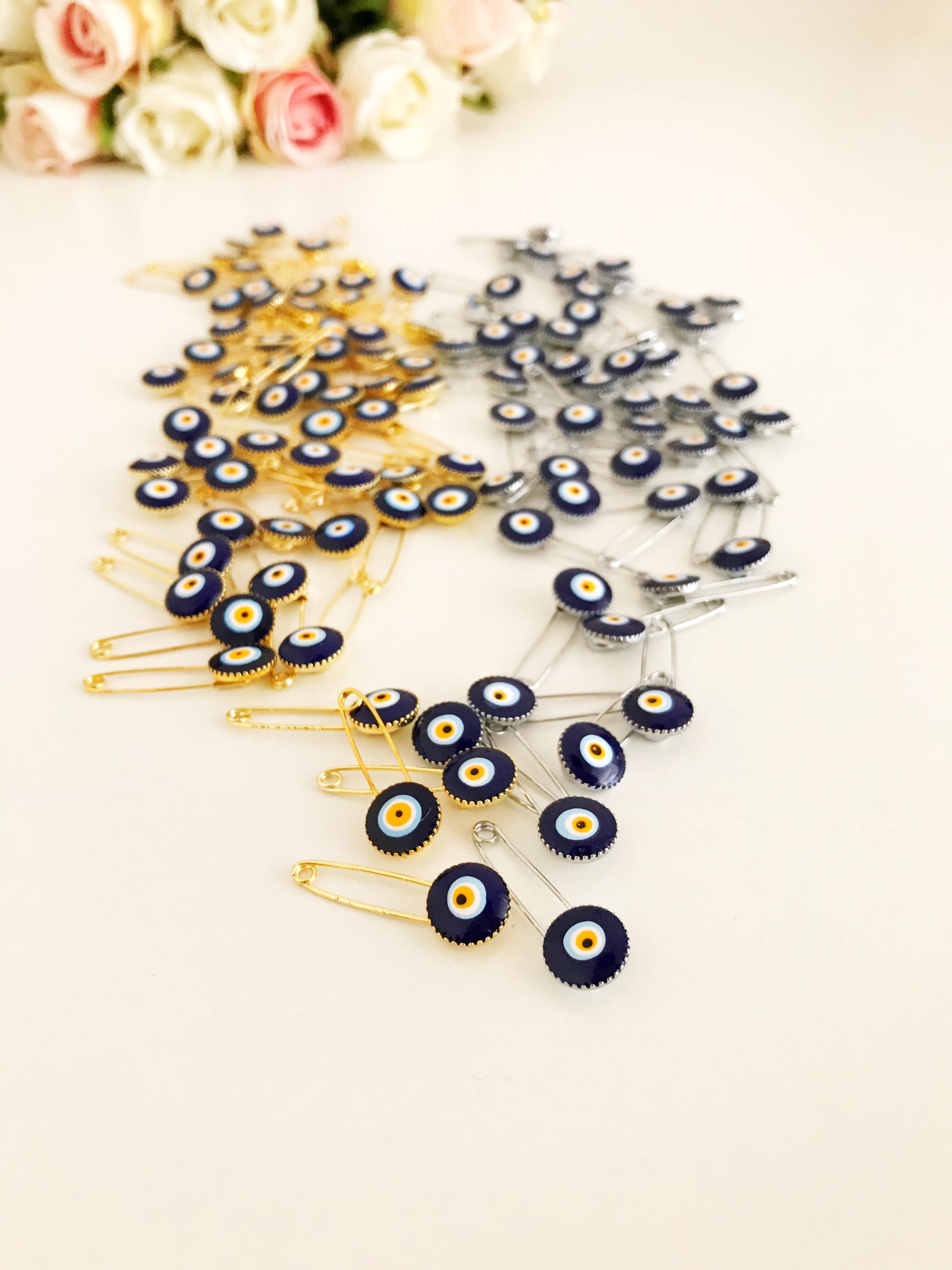 A collection of 100 blue evil eye safety pins, featuring brass construction and blue evil eye beads, ideal for weddings and baby showers.