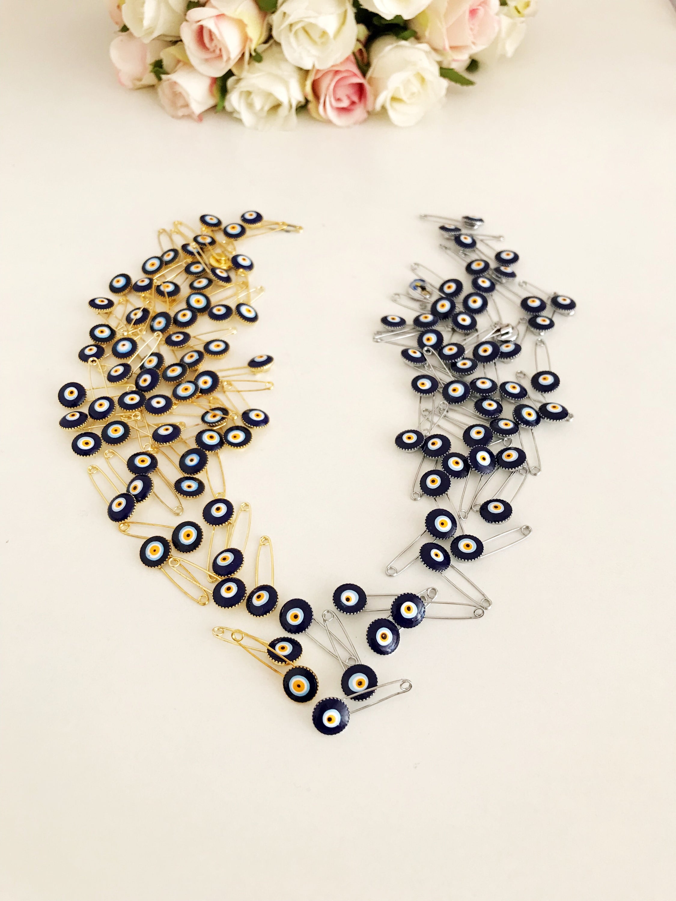 A collection of 100 blue evil eye safety pins, featuring brass construction and blue evil eye beads, ideal for weddings and baby showers.