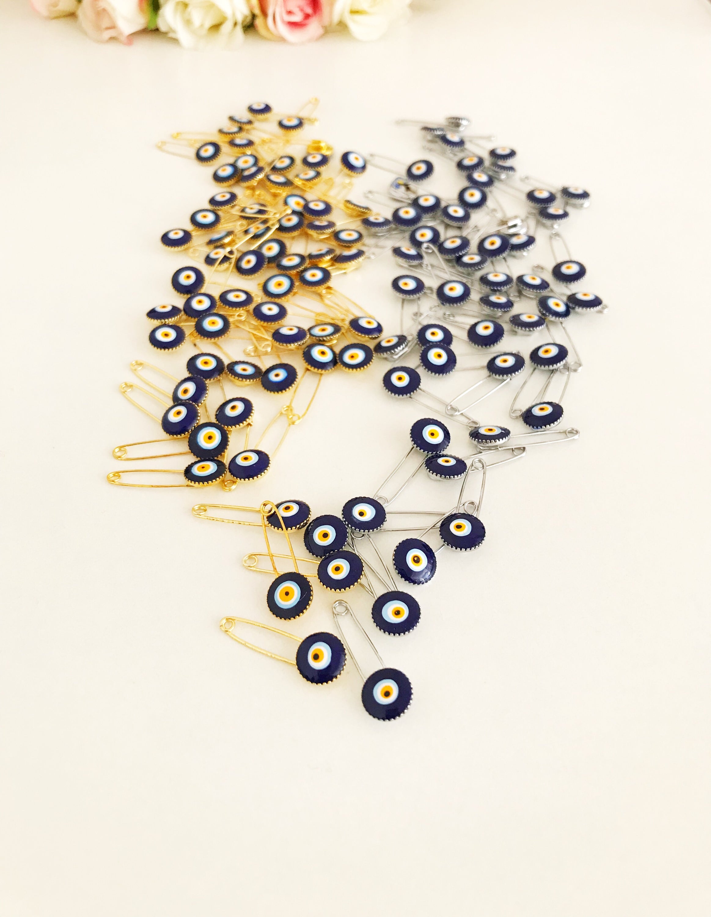 A collection of 100 blue evil eye safety pins, featuring brass construction and blue evil eye beads, ideal for weddings and baby showers.