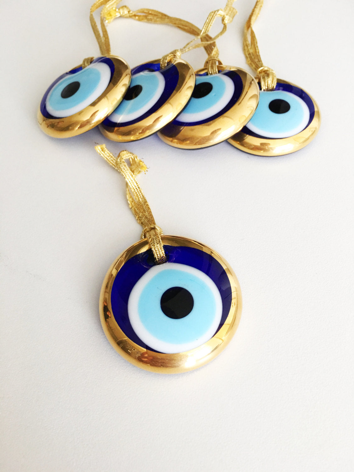 A set of 10 handmade evil eye charms featuring gold glass beads, ready for wall hanging or car decor, showcasing unique designs.