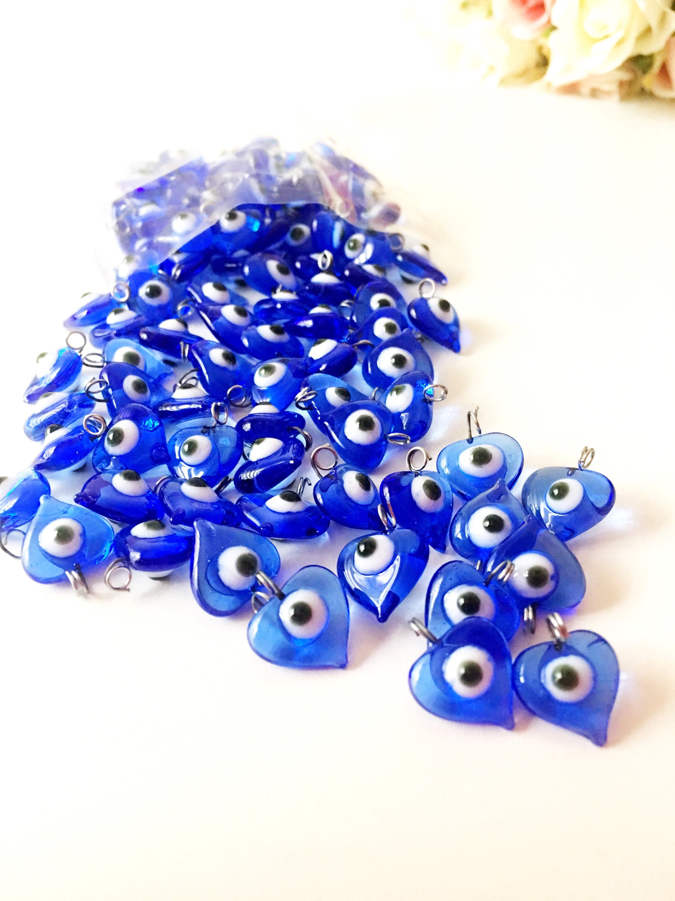 A collection of 100 unique blue evil eye charms with hooks, perfect for wedding favors and baby showers, displayed elegantly.