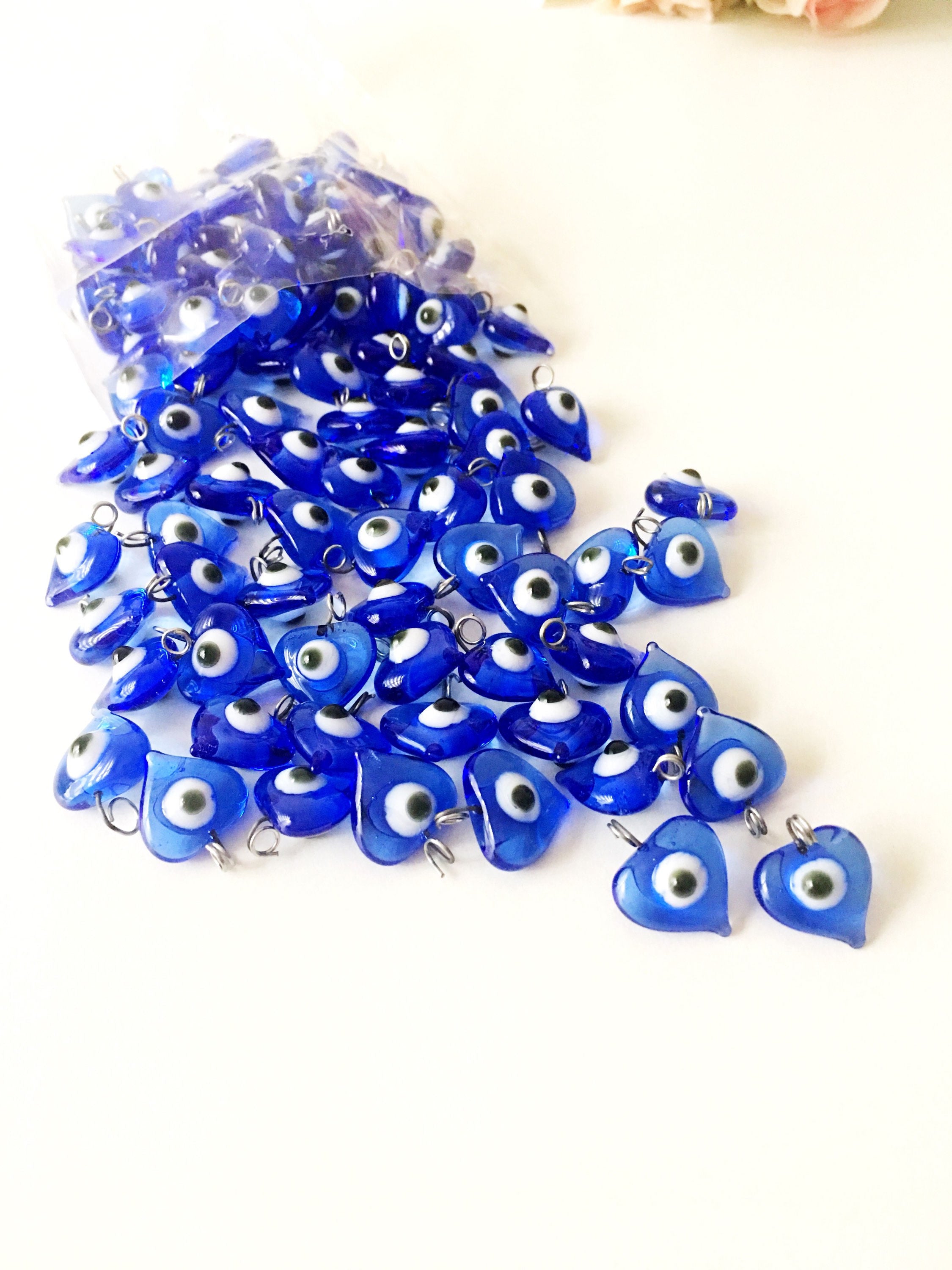 A collection of 100 unique blue evil eye charms with hooks, perfect for wedding favors and baby showers, displayed elegantly.