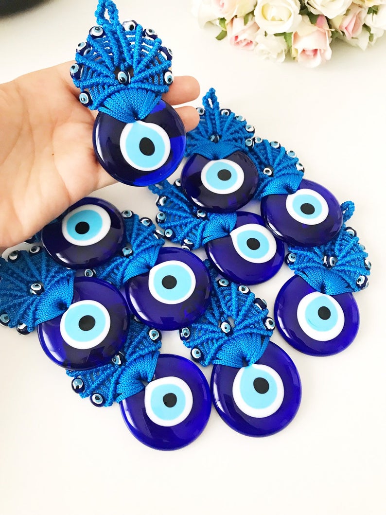 A beautifully handcrafted blue macrame wall hanging featuring a large Greek evil eye bead and smaller plastic evil eye beads, perfect as wedding favors.