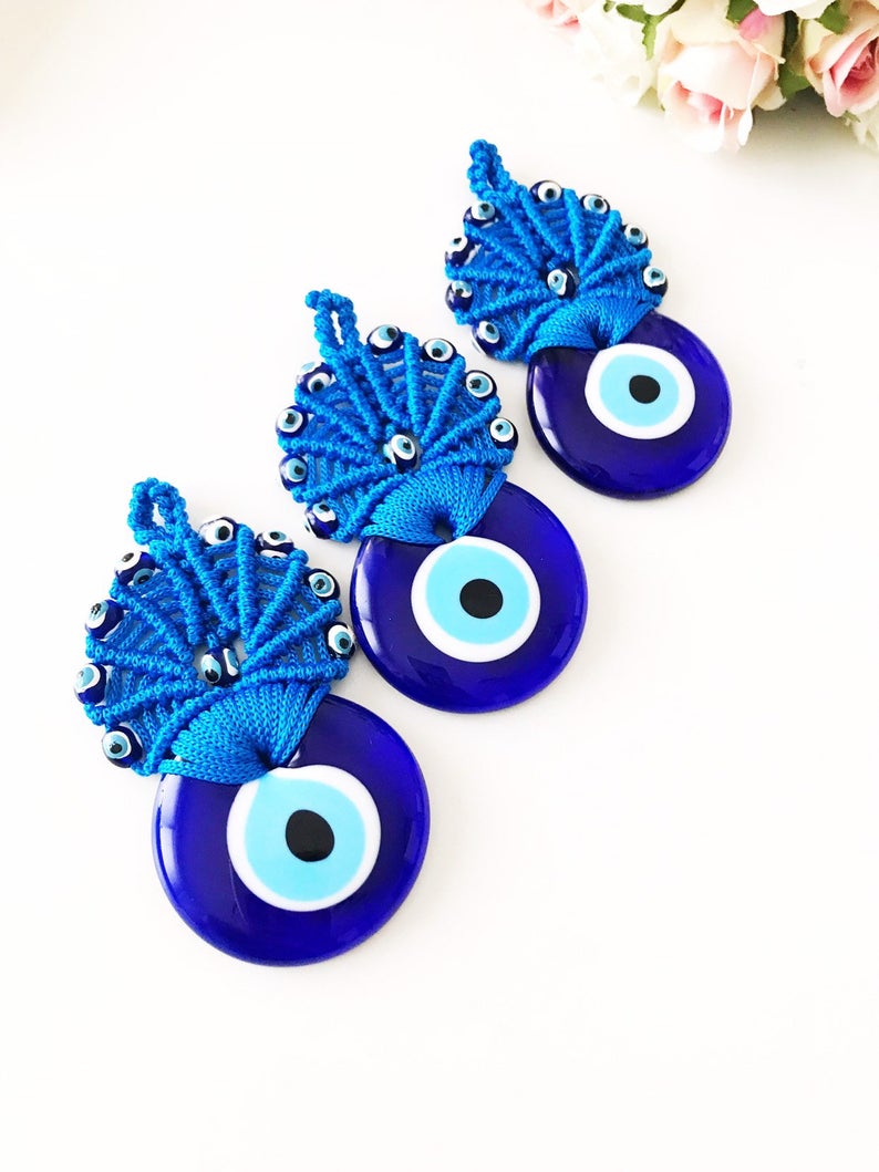 A beautifully handcrafted blue macrame wall hanging featuring a large Greek evil eye bead and smaller plastic evil eye beads, perfect as wedding favors.