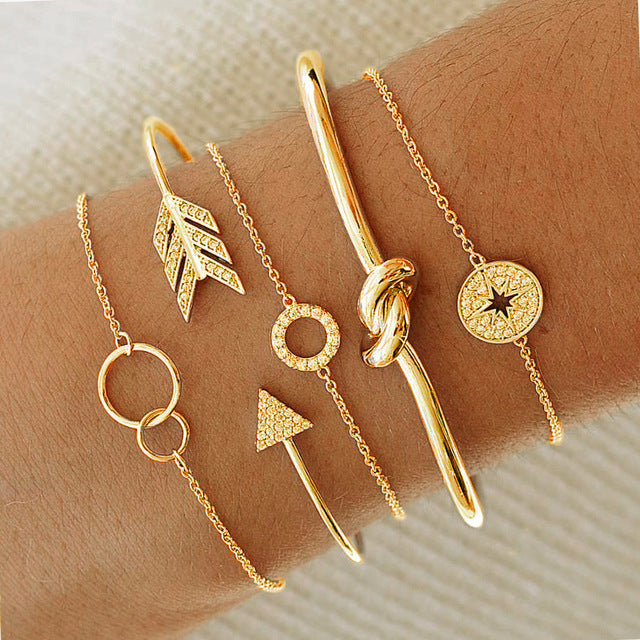 A stylish 5-piece bangle set featuring twisted knot designs, plated in 14K gold with sparkling cubic zirconia accents.