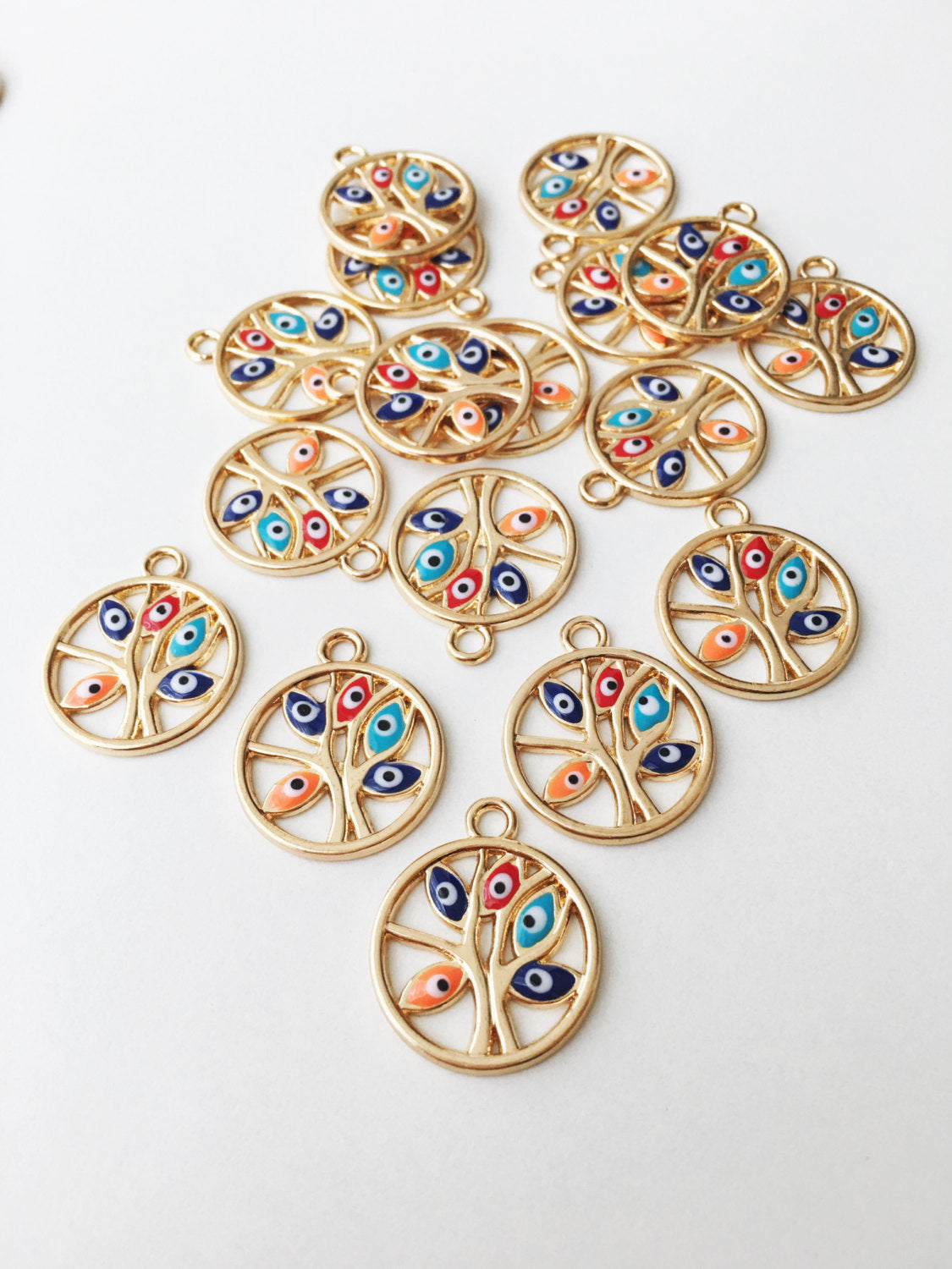 Two gold plated tree of life evil eye charms with colorful enamel designs, showcasing intricate details and a protective symbol.