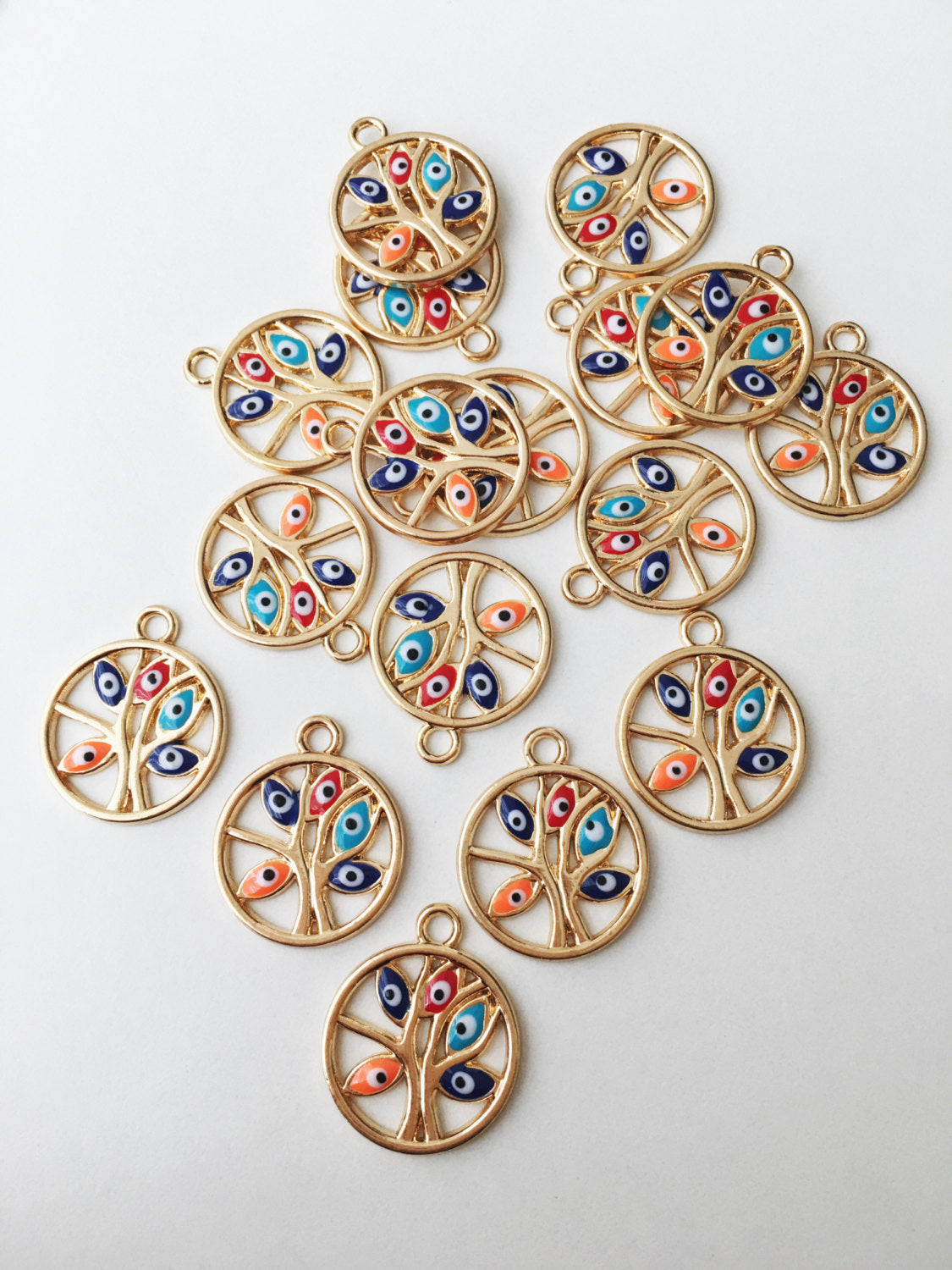 Two gold plated tree of life evil eye charms with colorful enamel designs, showcasing intricate details and a protective symbol.