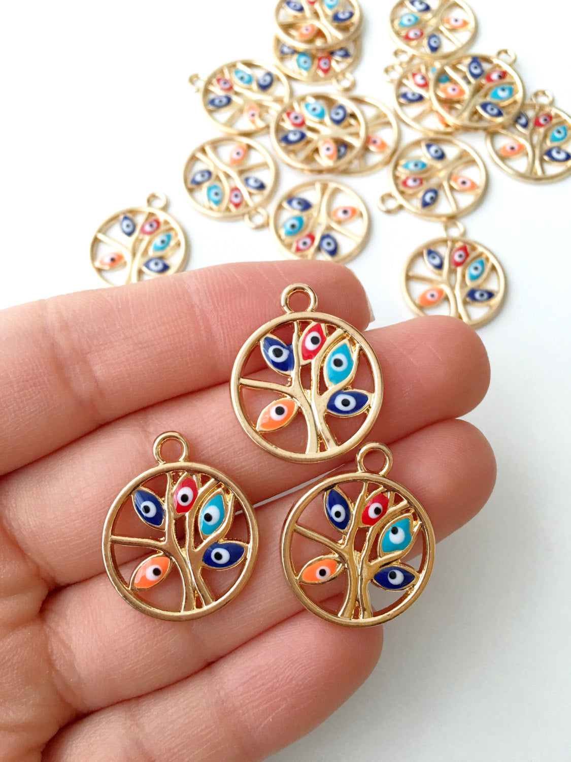 Two gold plated tree of life evil eye charms with colorful enamel designs, showcasing intricate details and a protective symbol.