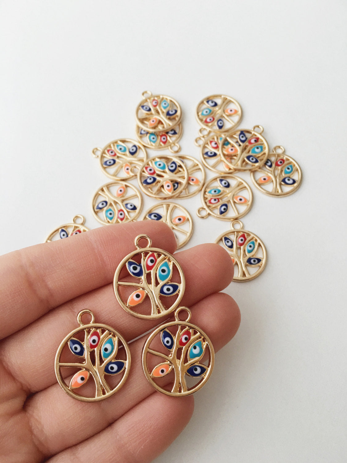 Two gold plated tree of life evil eye charms with colorful enamel designs, showcasing intricate details and a protective symbol.