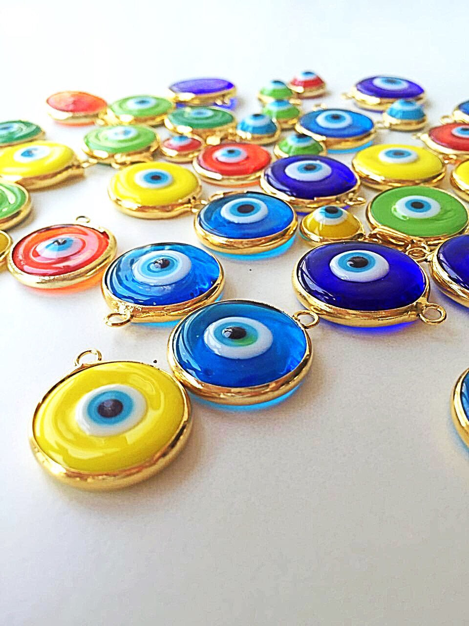 A collection of 22mm glass evil eye charms in various colors, featuring a matte 22K gold plated finish, perfect for jewelry making.