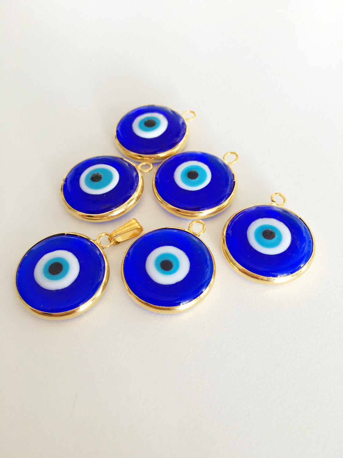 Two gold plated evil eye pendants, 22mm diameter, featuring dark blue and opaque blue glass charms, showcasing intricate Turkish craftsmanship.