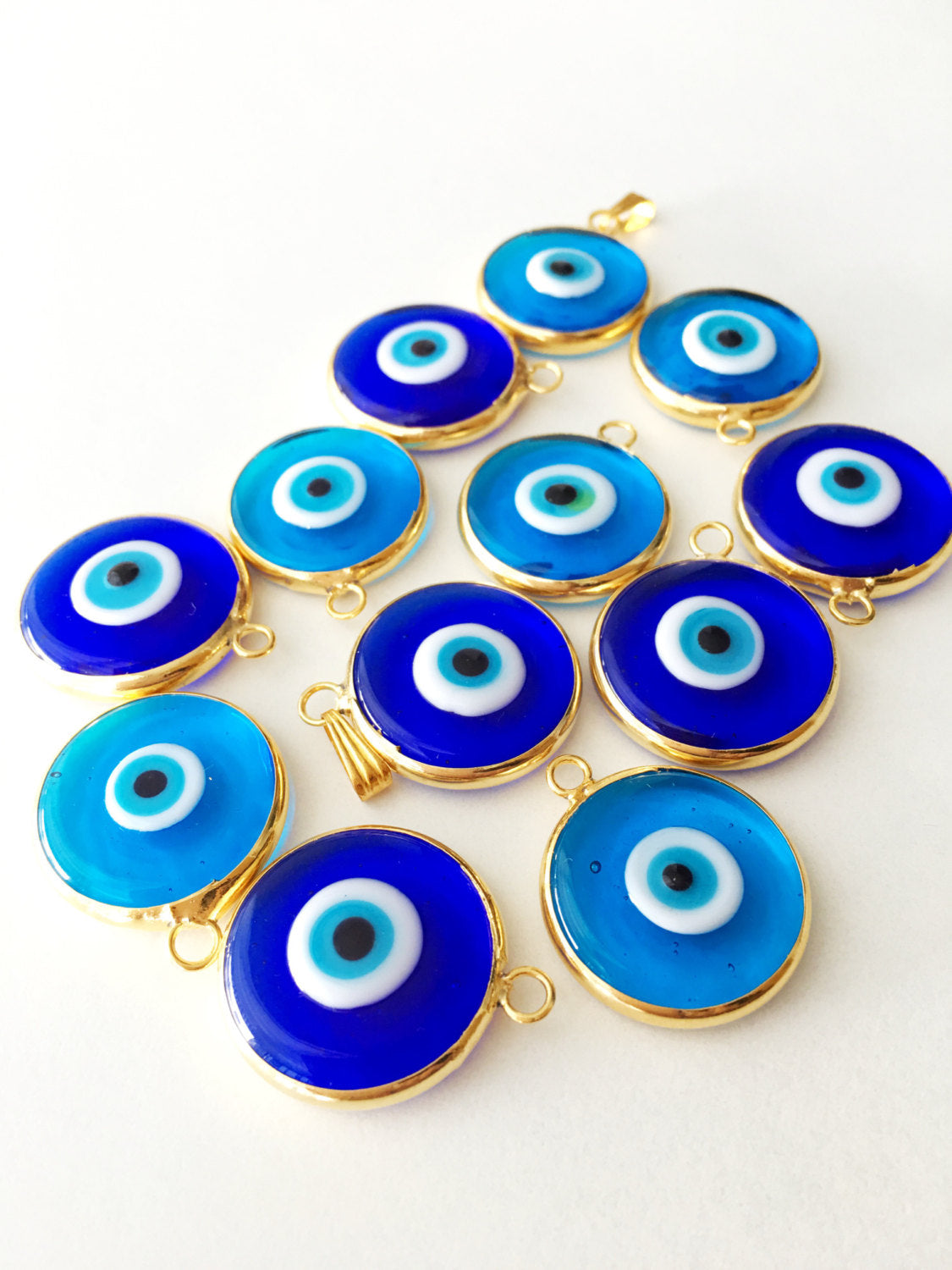 Two gold plated evil eye pendants, 22mm diameter, featuring dark blue and opaque blue glass charms, showcasing intricate Turkish craftsmanship.