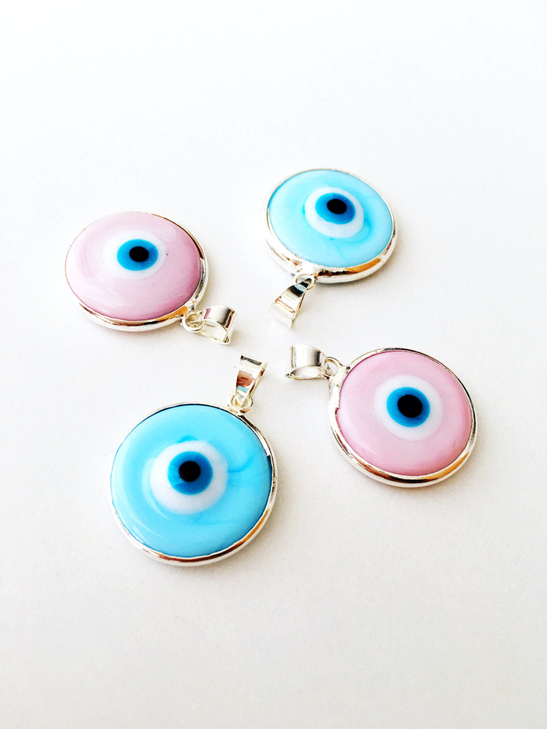 Two silver plated evil eye pendants in baby blue and baby pink, showcasing Murano glass craftsmanship.