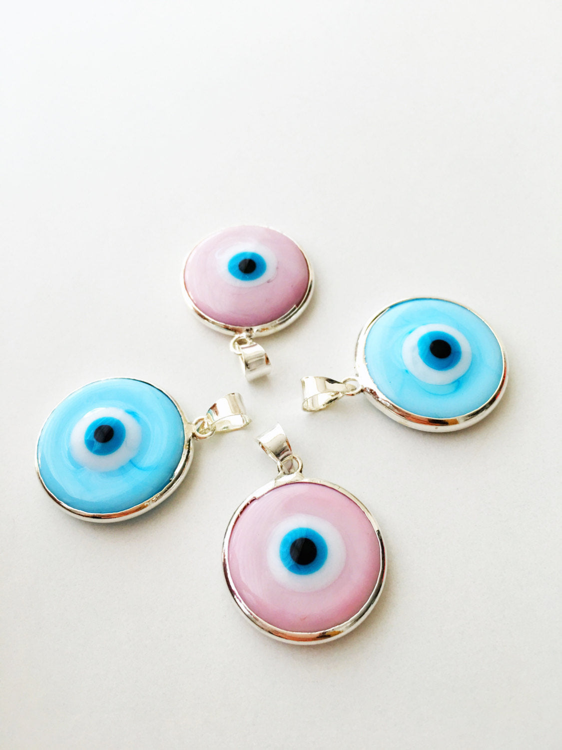 Two silver plated evil eye pendants in baby blue and baby pink, showcasing Murano glass craftsmanship.