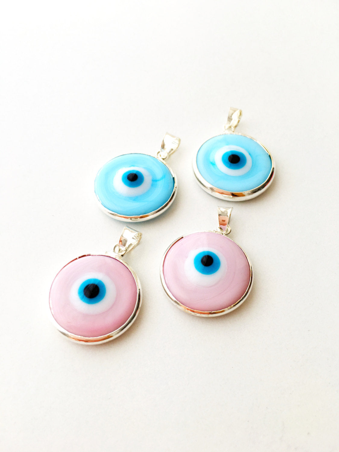 Two silver plated evil eye pendants in baby blue and baby pink, showcasing Murano glass craftsmanship.