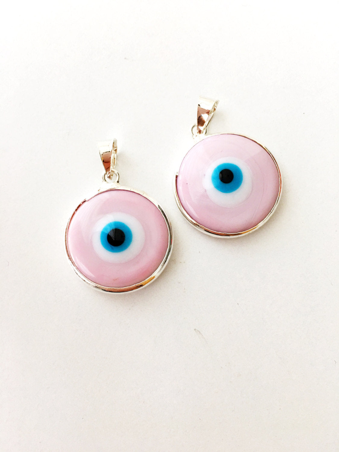 Two silver plated evil eye pendants in baby blue and baby pink, showcasing Murano glass craftsmanship.