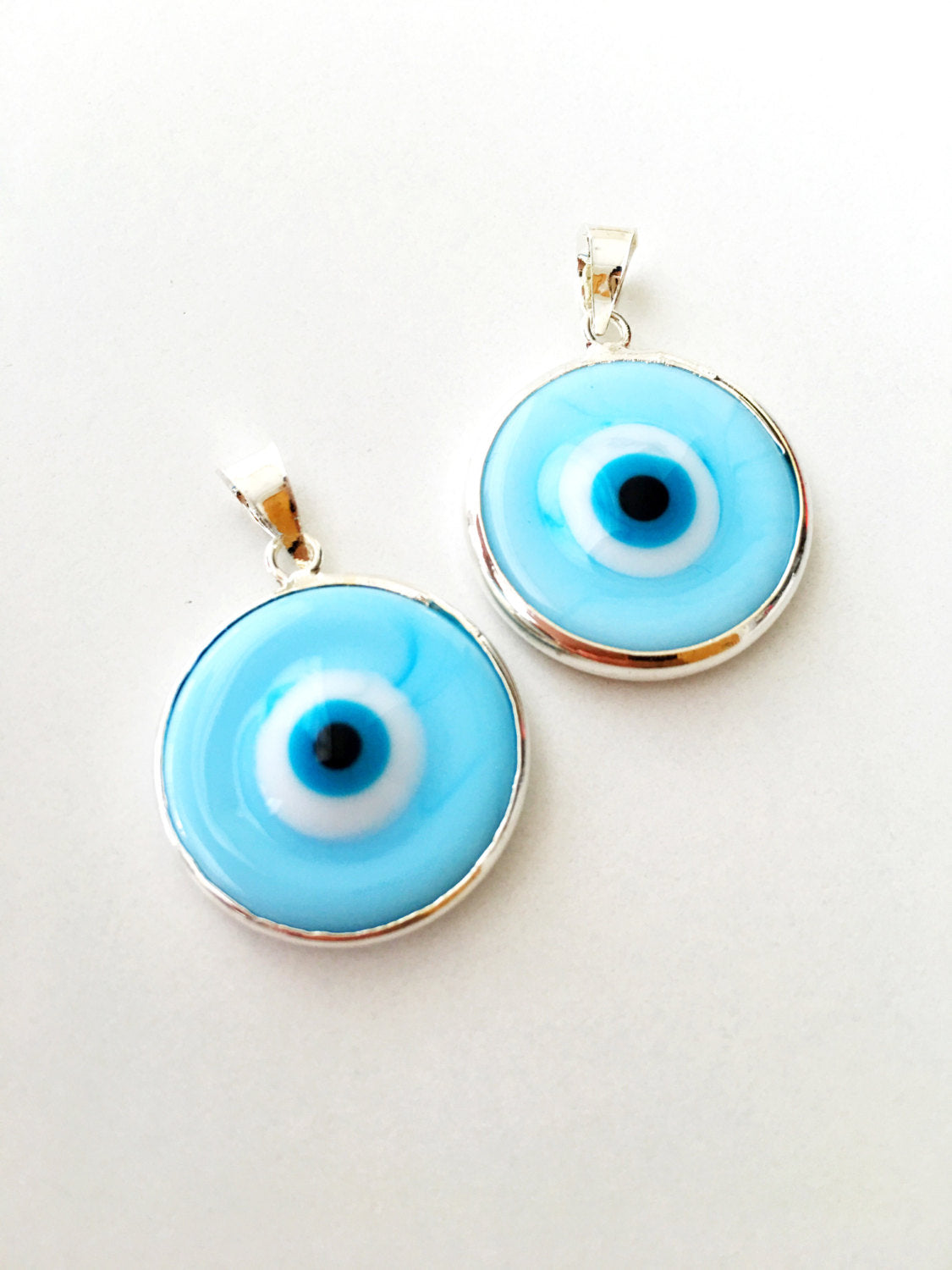 Two silver plated evil eye pendants in baby blue and baby pink, showcasing Murano glass craftsmanship.