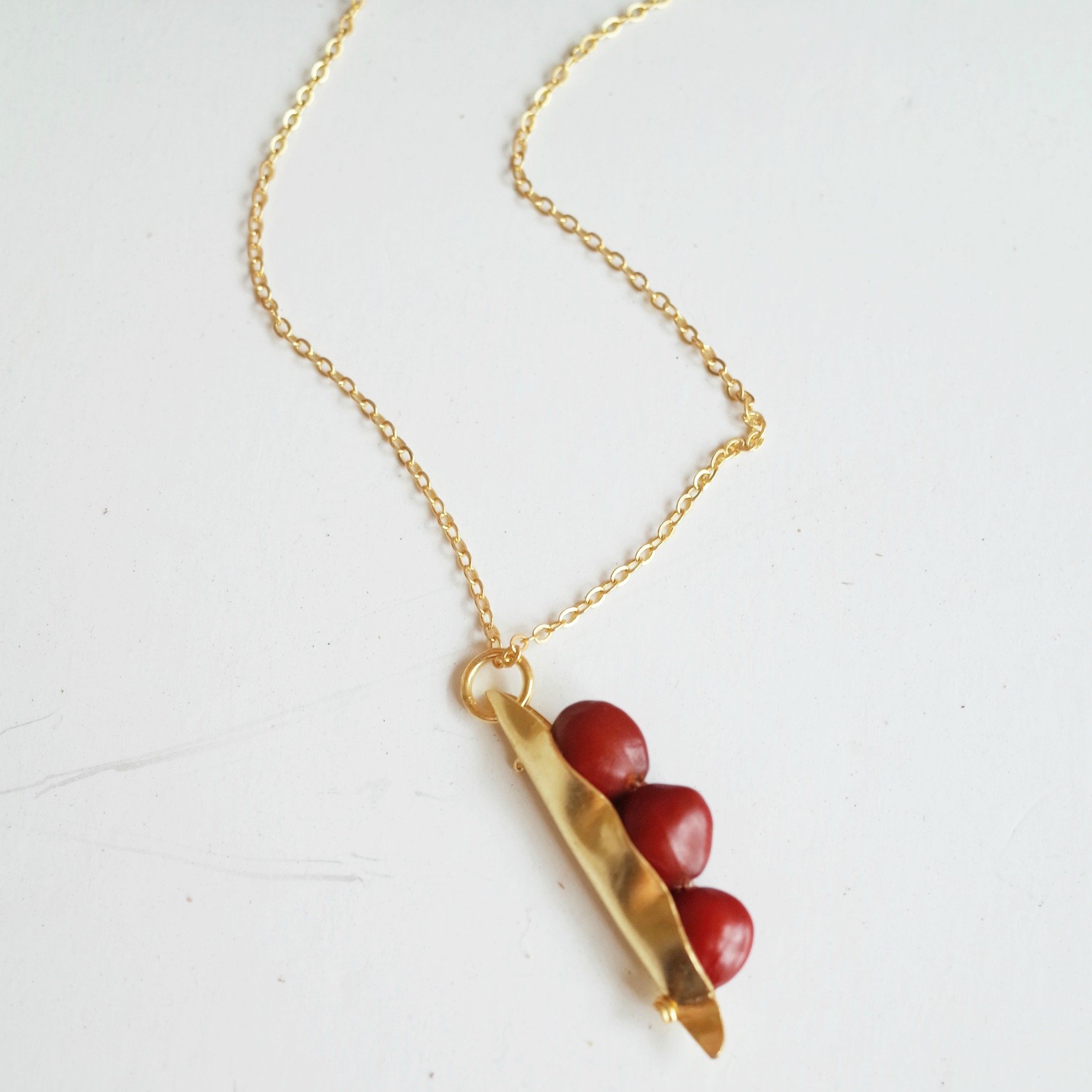 A handcrafted 3 Seeds in a Pod Pendant featuring natural Manjadi Kuru seeds on a gold plated chain, showcasing vibrant colors.