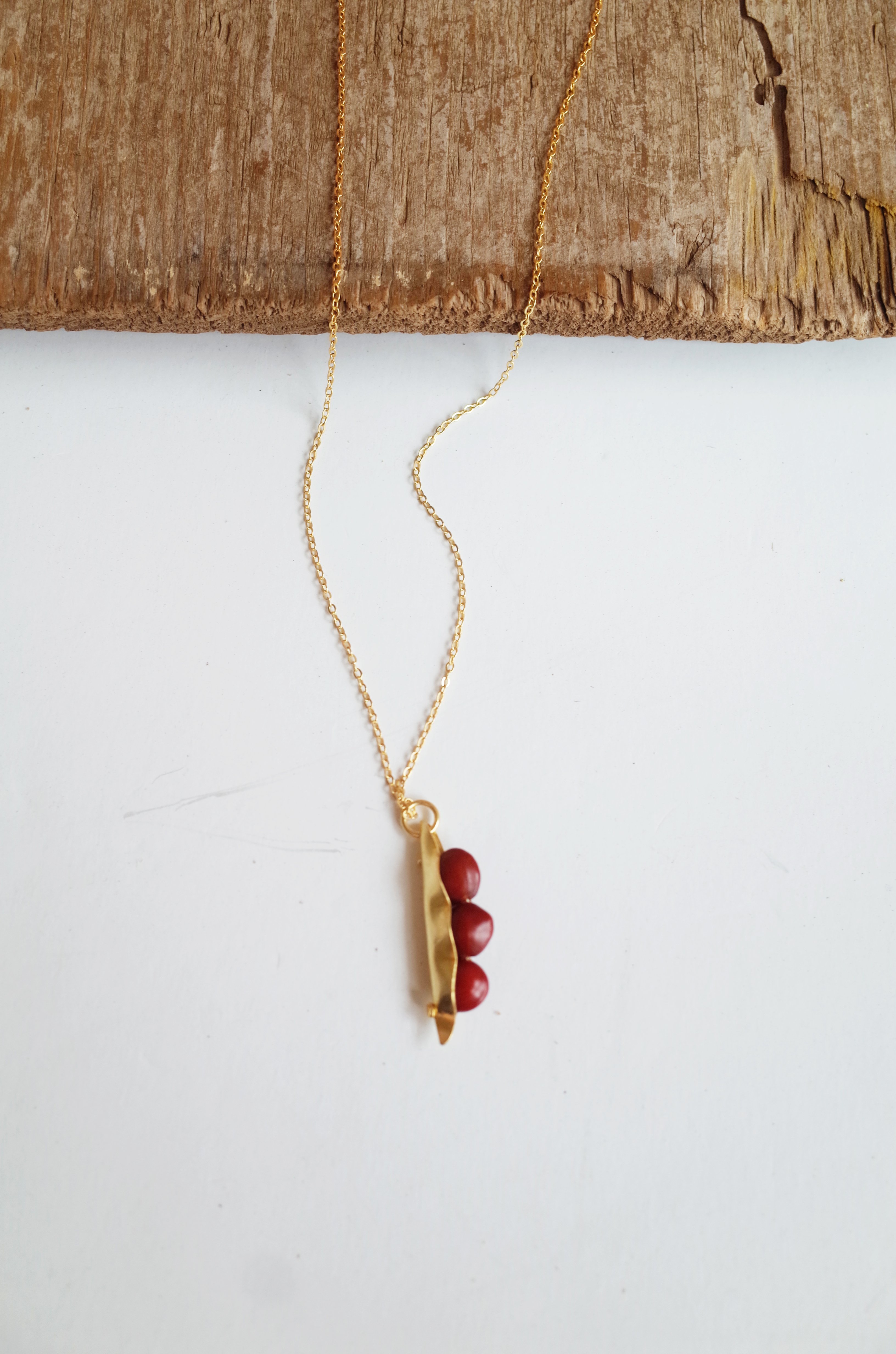 A handcrafted 3 Seeds in a Pod Pendant featuring natural Manjadi Kuru seeds on a gold plated chain, showcasing vibrant colors.