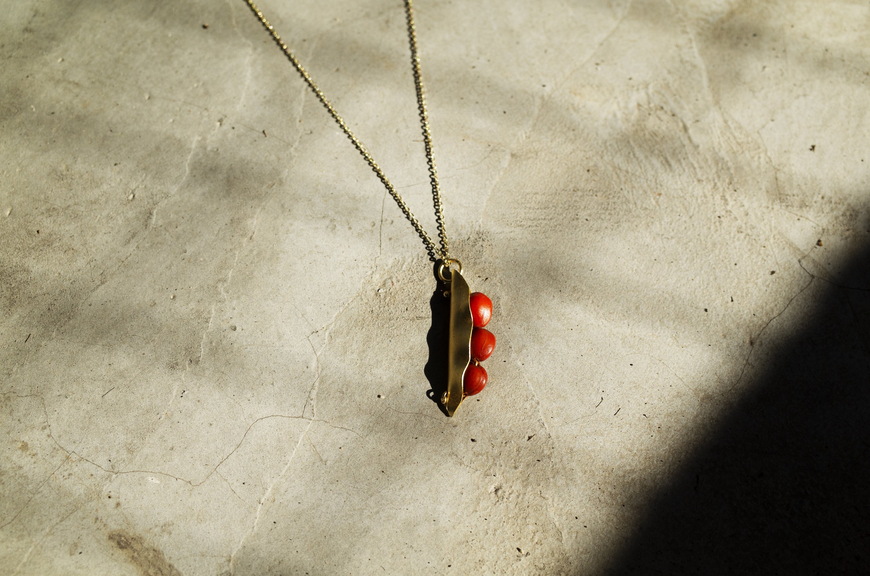 A handcrafted 3 Seeds in a Pod Pendant featuring natural Manjadi Kuru seeds on a gold plated chain, showcasing vibrant colors.