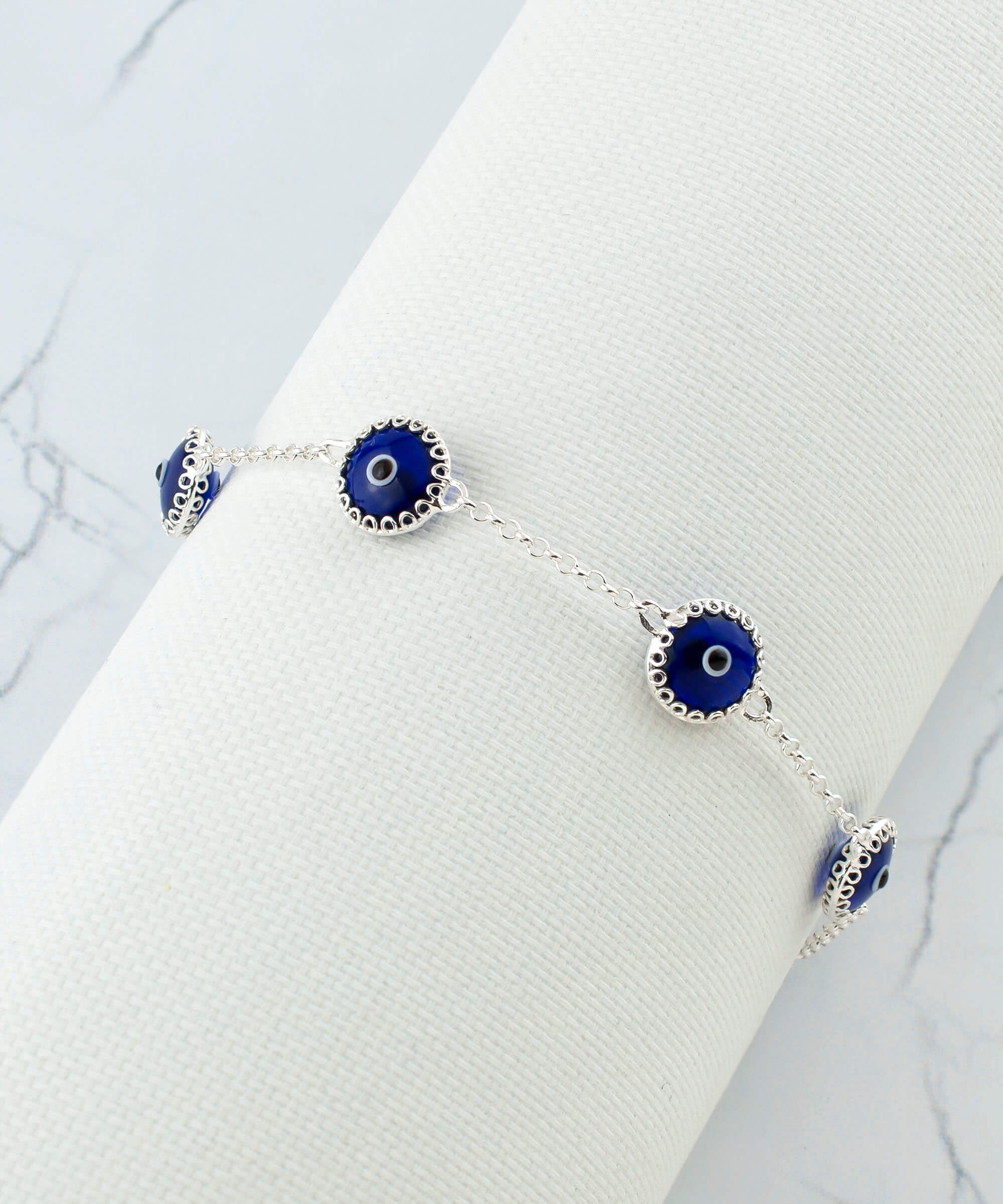 A stylish sterling silver link bracelet featuring five dark blue evil eye beads, designed for women, showcasing a secure lobster claw clasp.