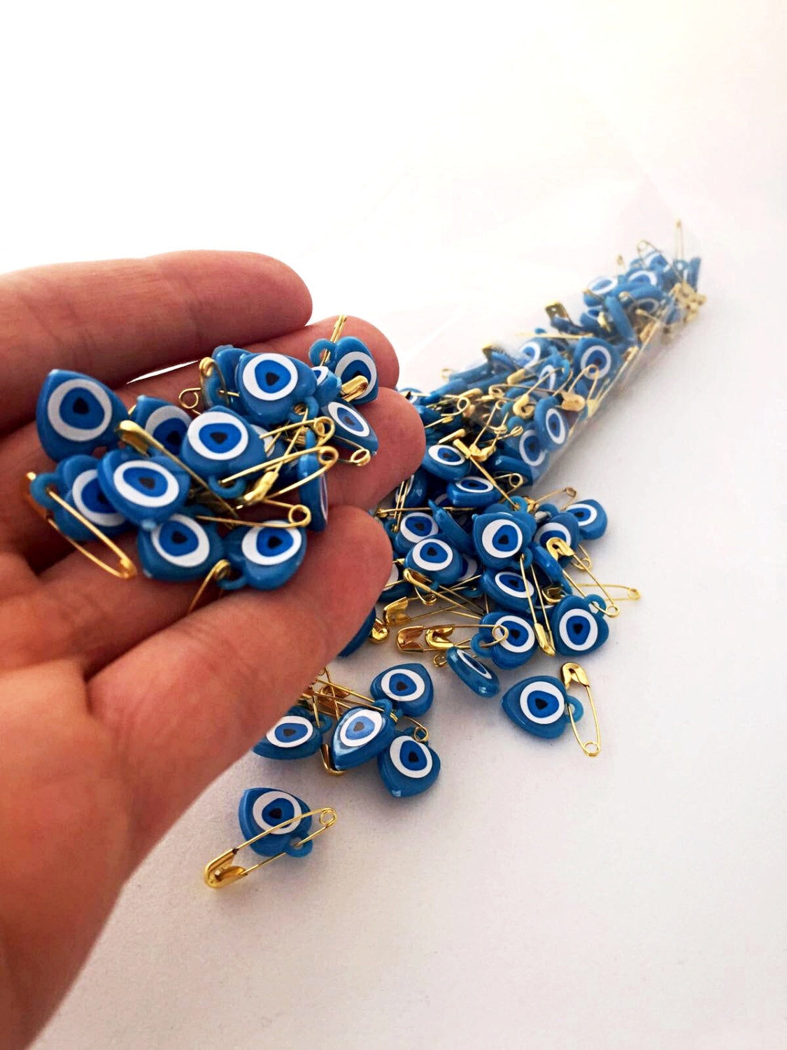 A collection of 100 pcs evil eye safety pins in various colors, featuring heart-shaped resin designs with evil eye beads.