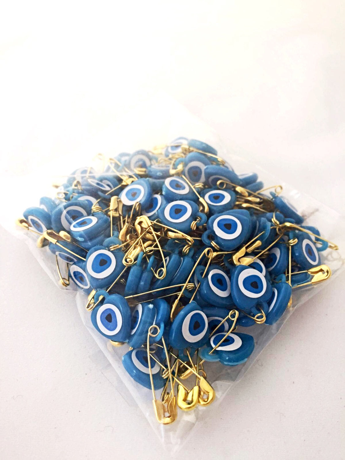 A collection of 100 pcs evil eye safety pins in various colors, featuring heart-shaped resin designs with evil eye beads.