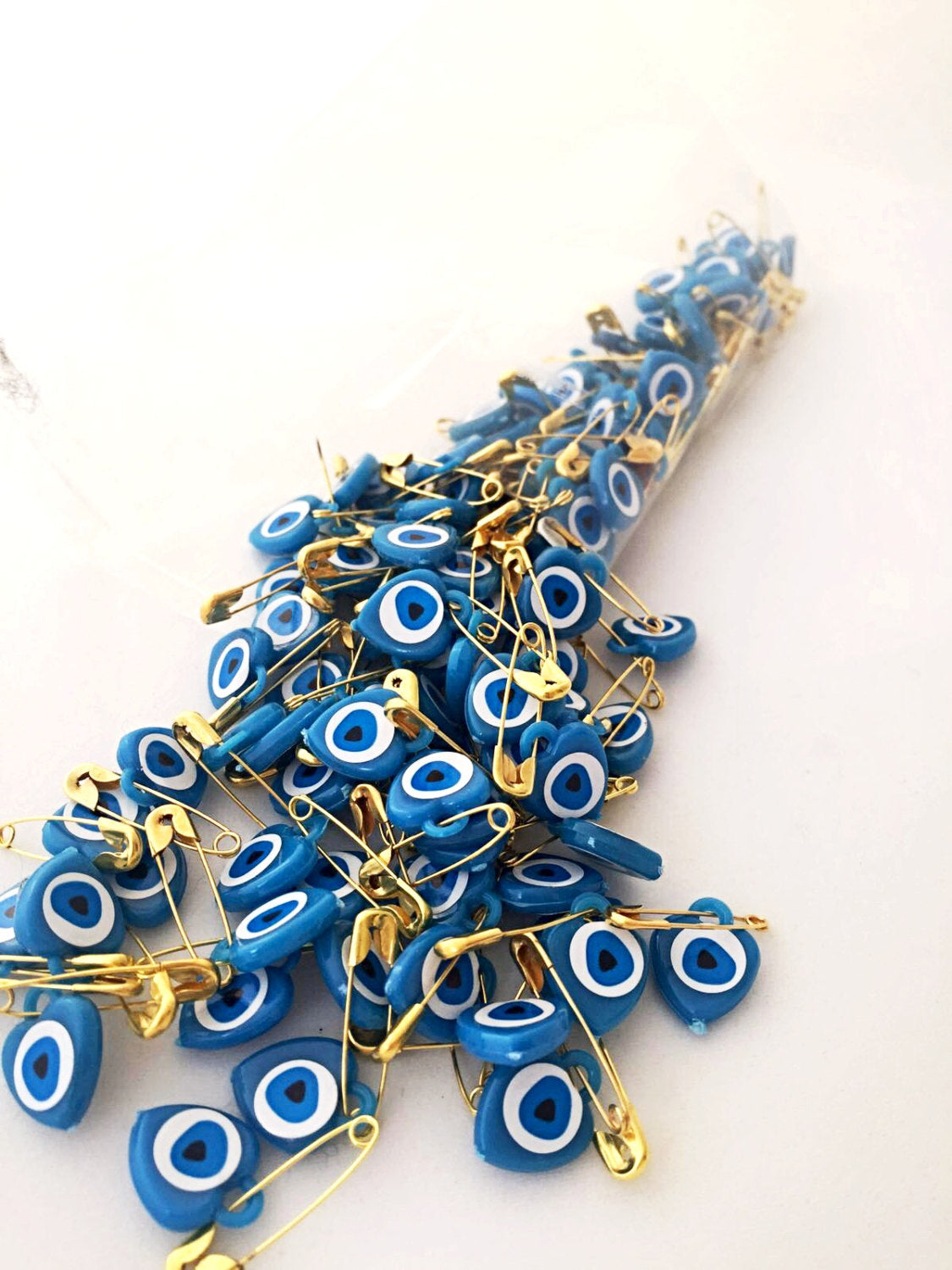 A collection of 100 pcs evil eye safety pins in various colors, featuring heart-shaped resin designs with evil eye beads.