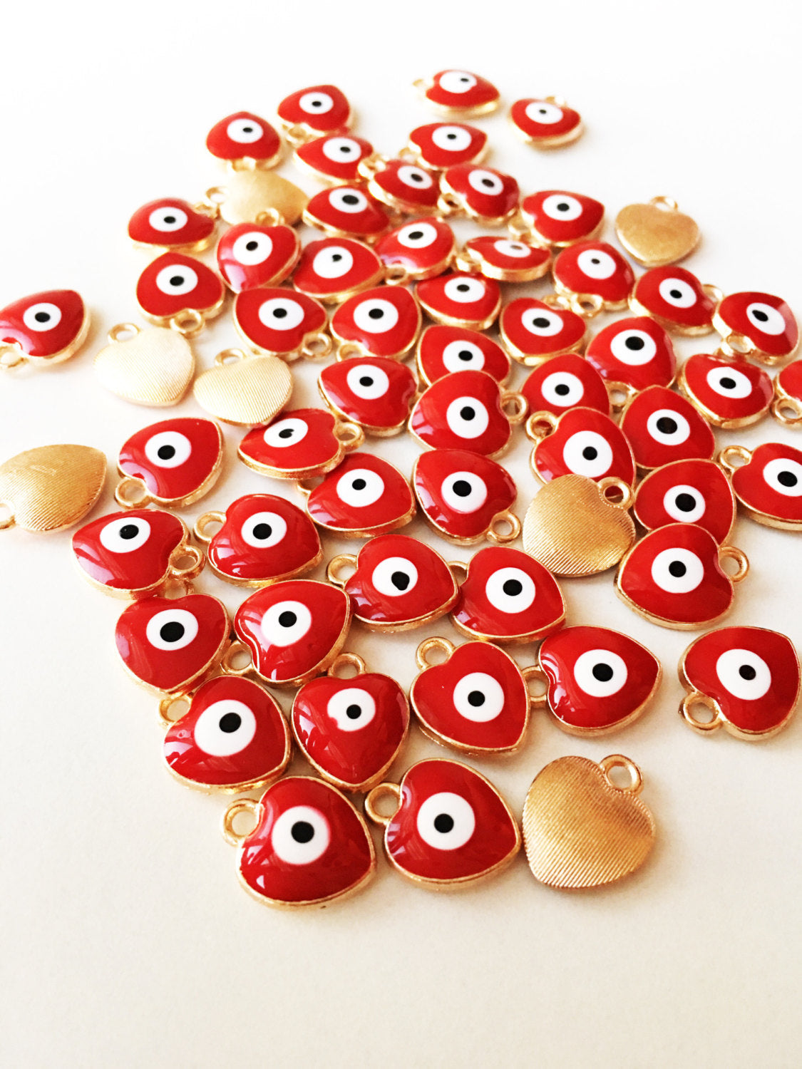 Five heart-shaped evil eye charms in dark blue, white, and red, featuring gold plating and enamel finish, ideal for jewelry making.