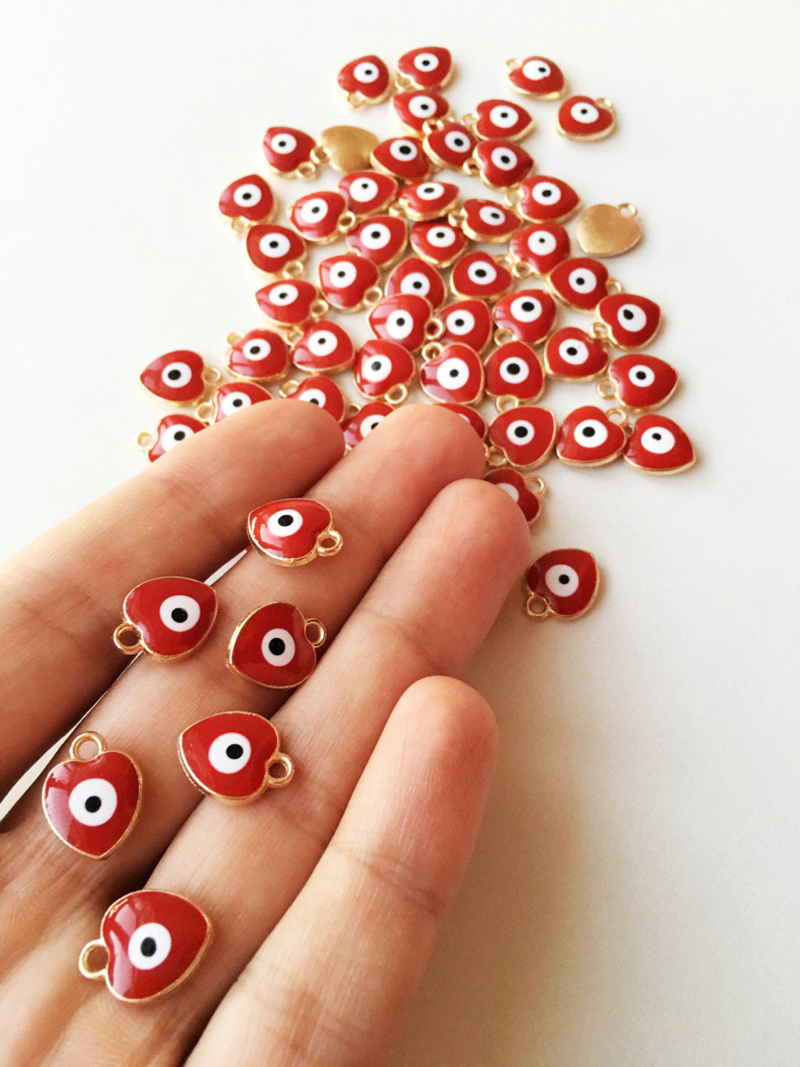 Five heart-shaped evil eye charms in dark blue, white, and red, featuring gold plating and enamel finish, ideal for jewelry making.