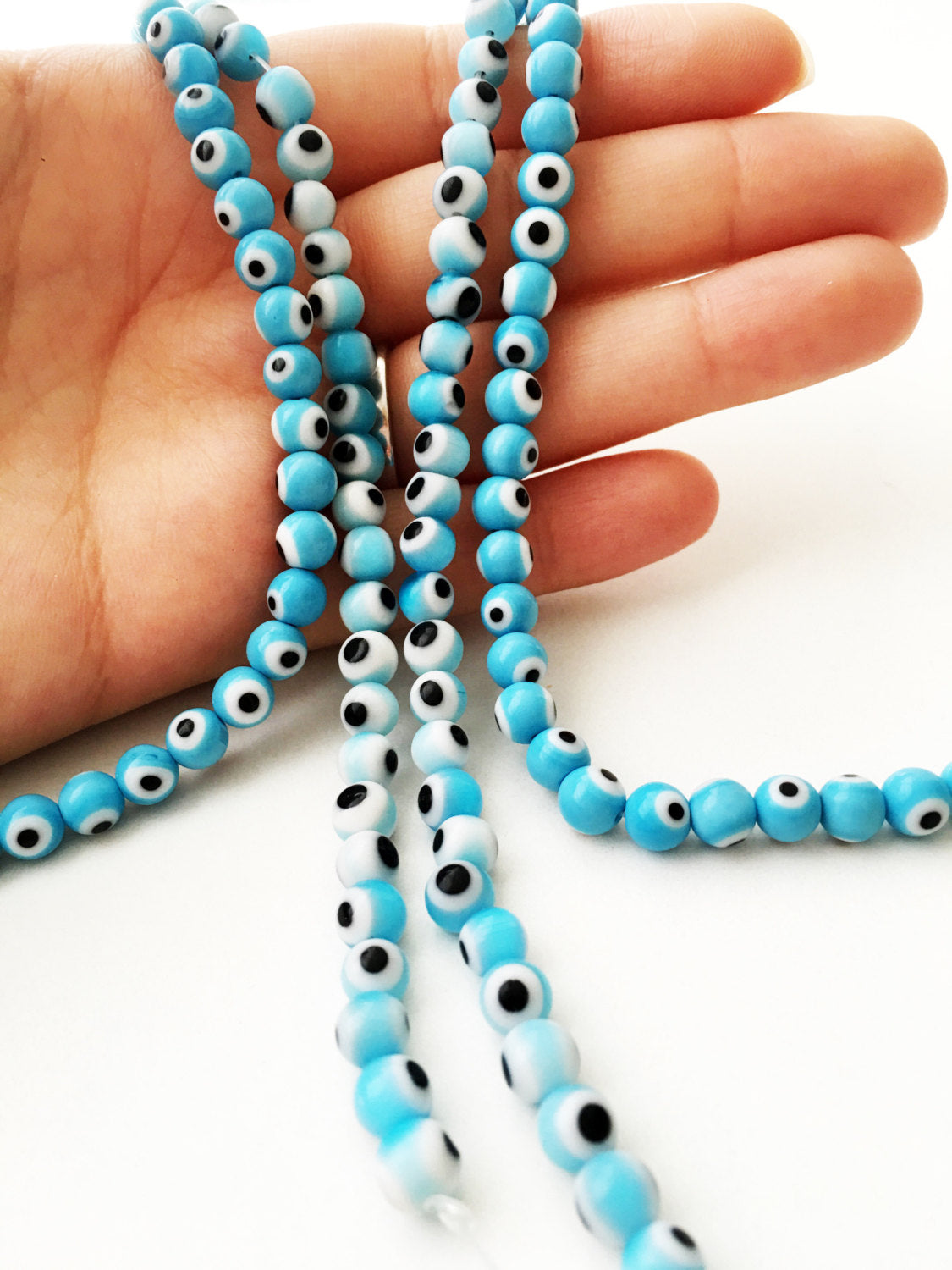 A strand of 6mm flat round baby blue glass evil eye beads, showcasing their unique handmade design.