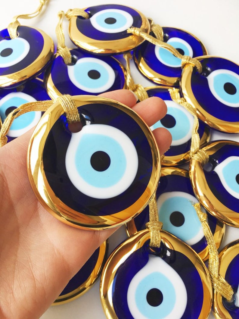 A 7cm handmade gold glass evil eye bead featuring a blue center and gold trim, symbolizing protection and good luck.