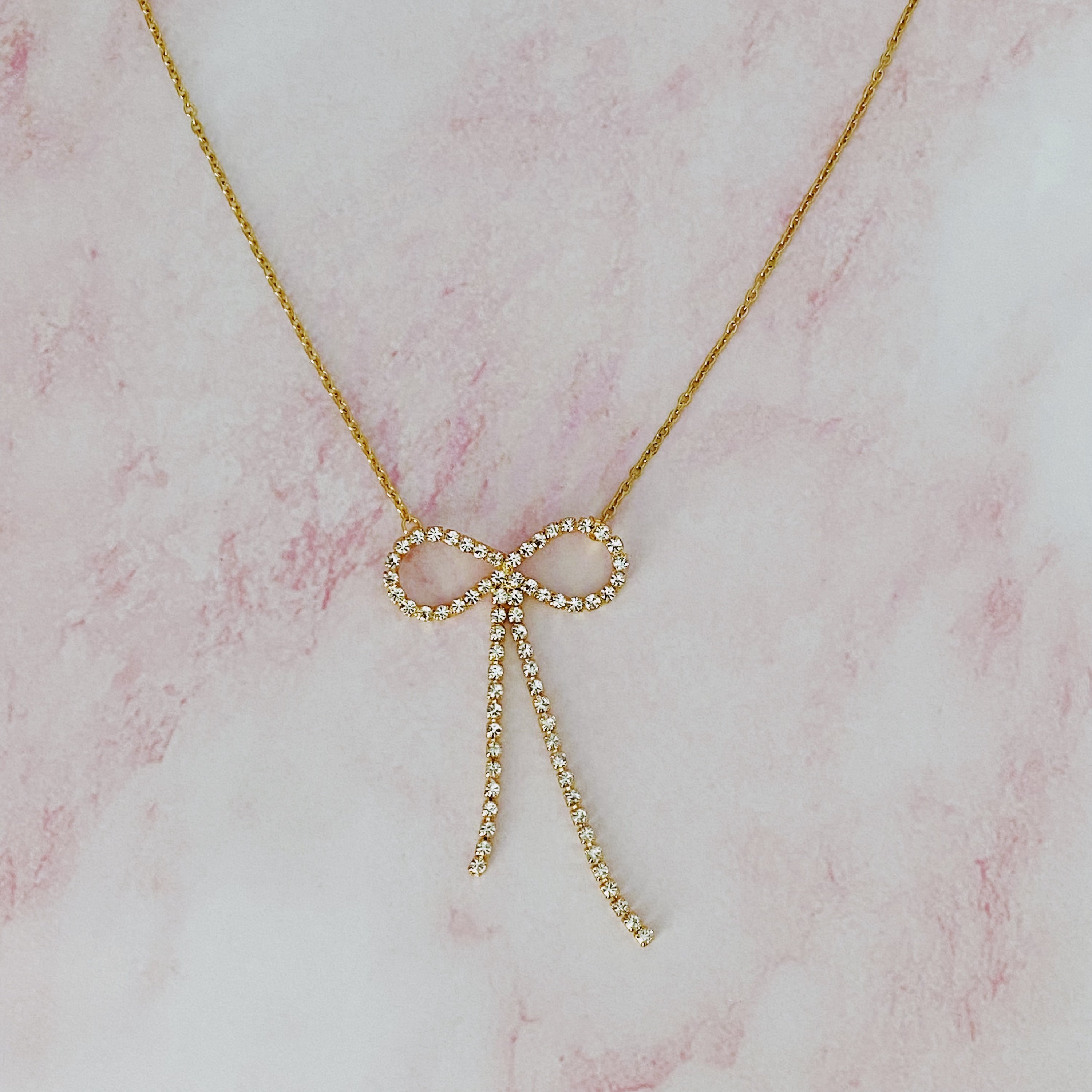 Adorable Shine Bow Necklace featuring a gold plated bow design with cubic zirconia accents, elegantly displayed on a soft background.