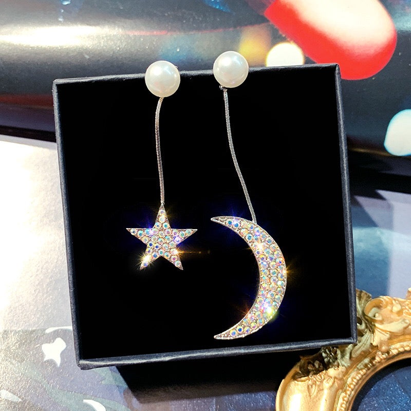 Asymmetric earrings featuring moon and star designs, adorned with pearls and rhinestones, showcasing a celestial theme.